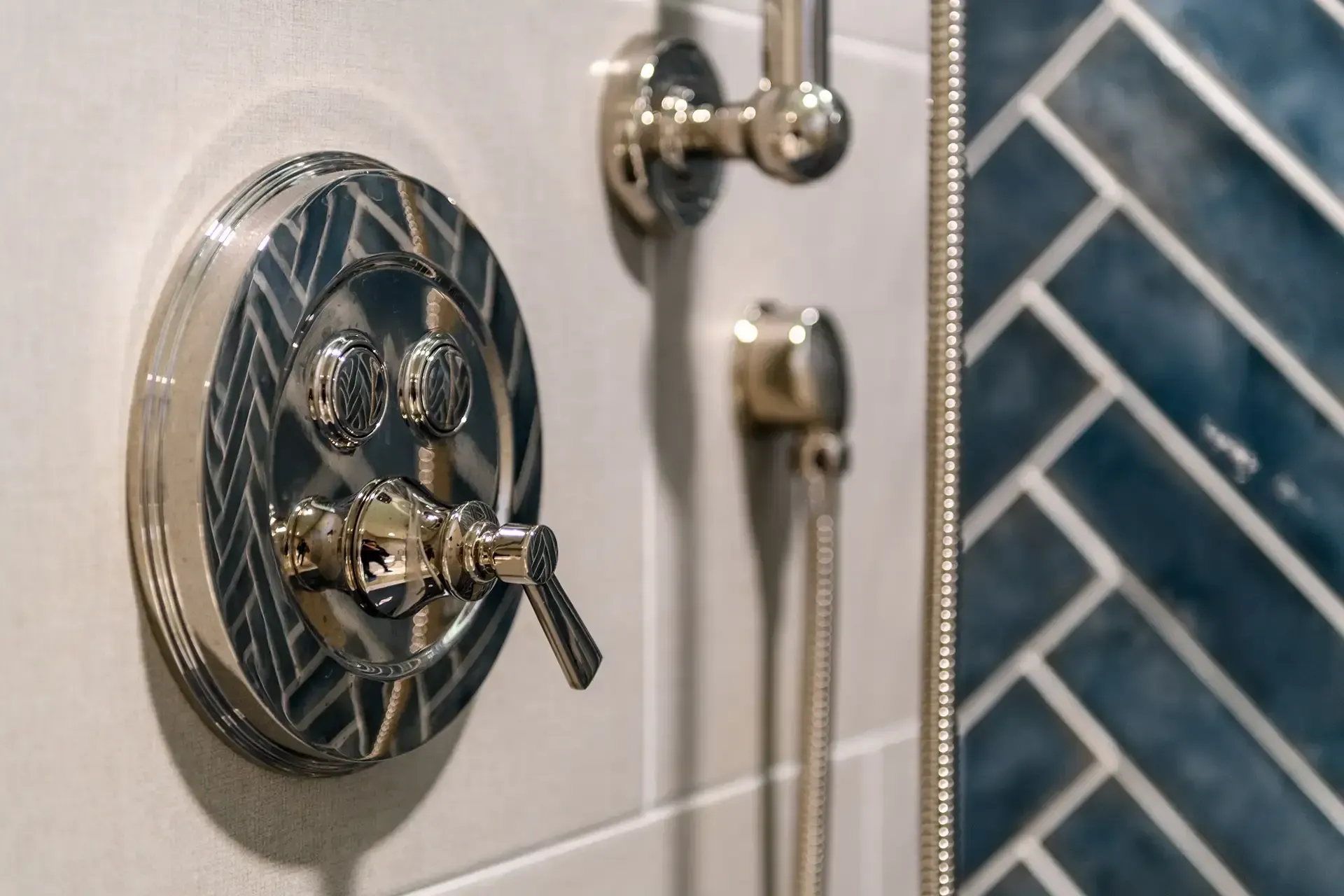 Shiny shower fixtures with a handle and two buttons on a white tiled wall, with blue herringbone tile.