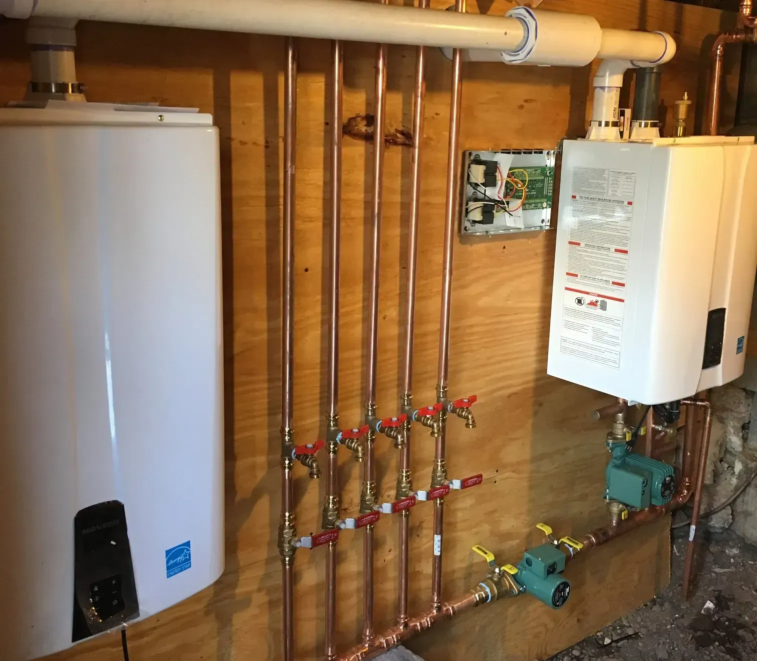 Plumbing with copper pipes and white water heaters on a wood wall.