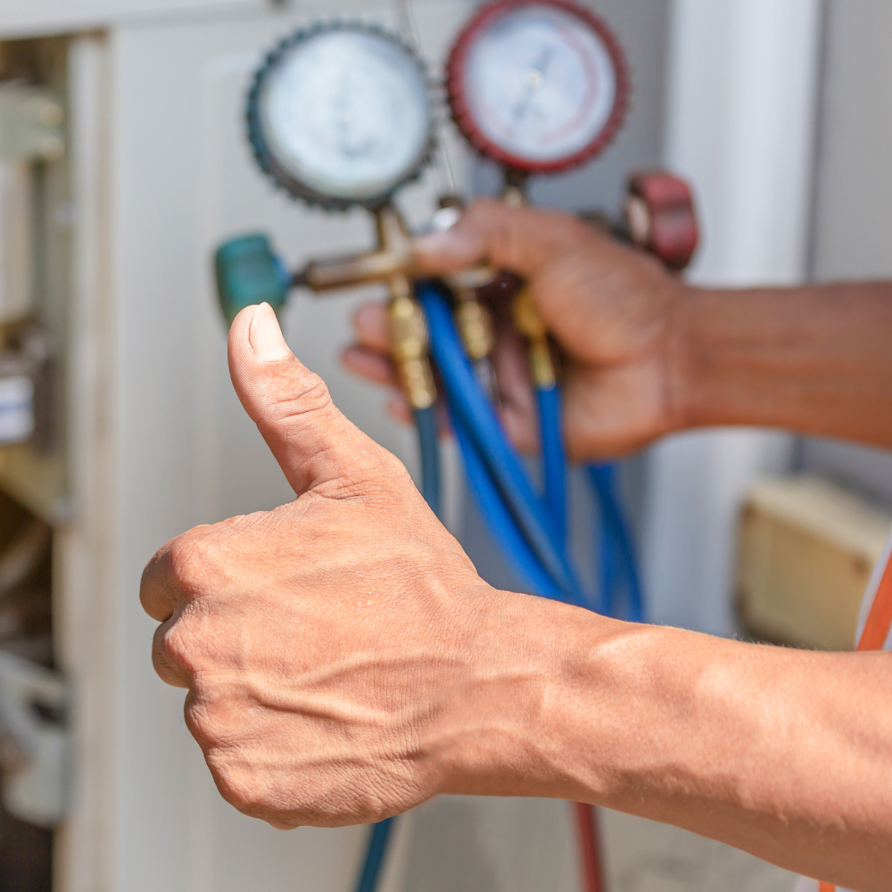 Hand with thumbs up, holding gauges with hoses, likely checking air conditioning unit.