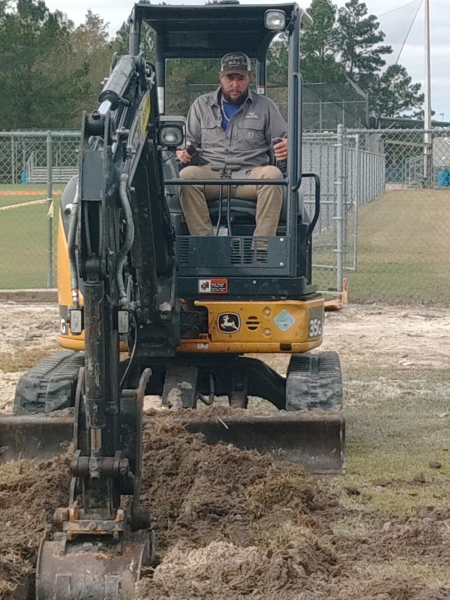 A man is driving a small excavator in a field.