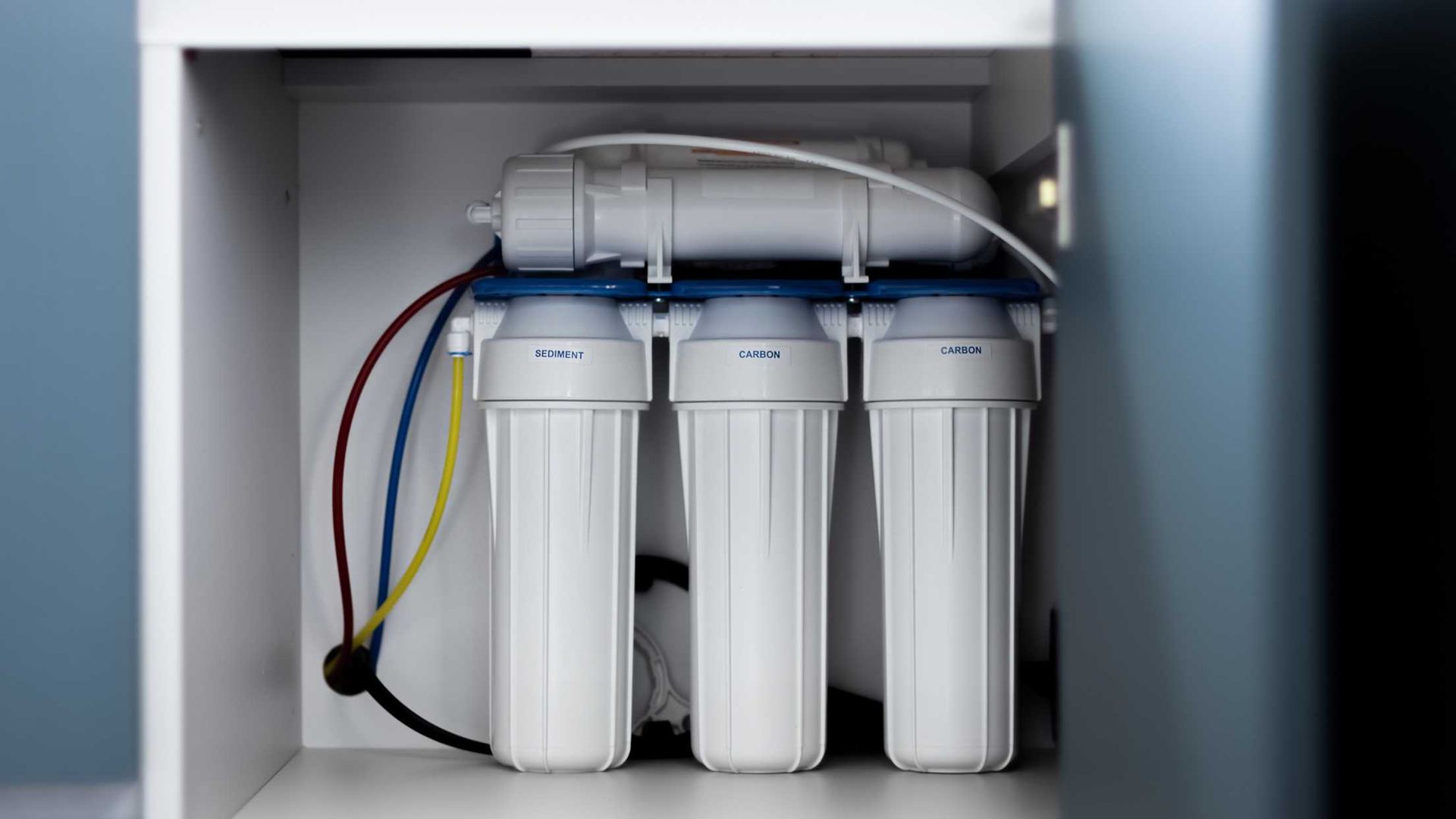 A water filter is sitting inside of a cabinet.