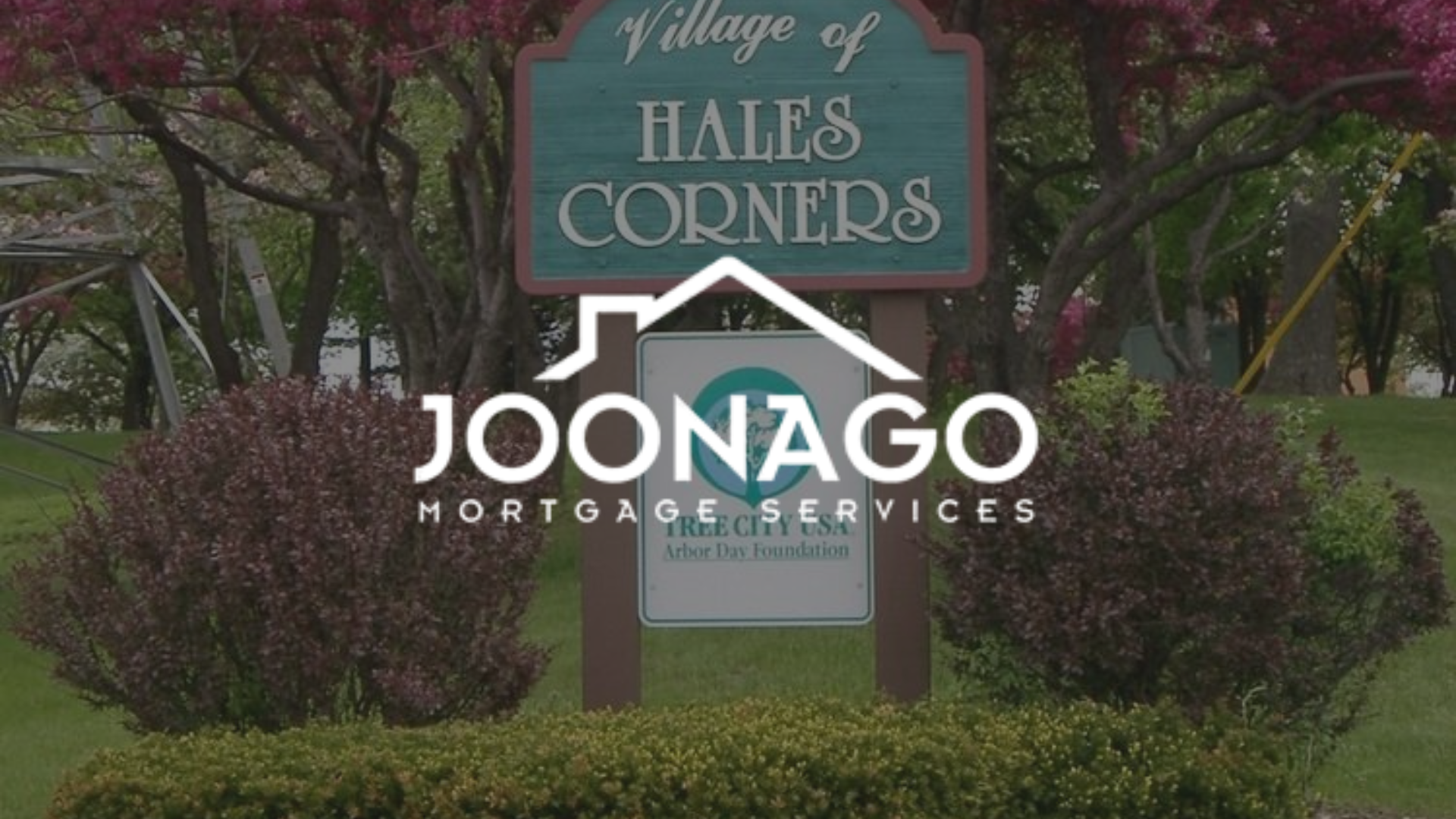 Sign for Hales Corners, Wisconsin, with a Joonago Mortgage Services logo in front.