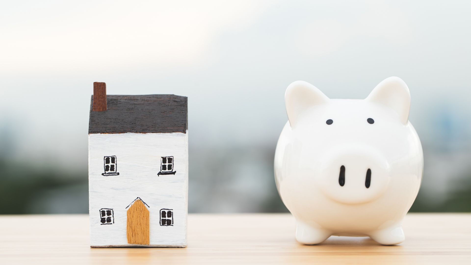 A piggy bank and a model house are on a wooden table.