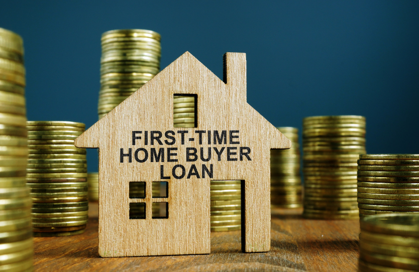 A wooden house with the words `` first time home buyer loan '' written on it is surrounded by stacks of gold coins.