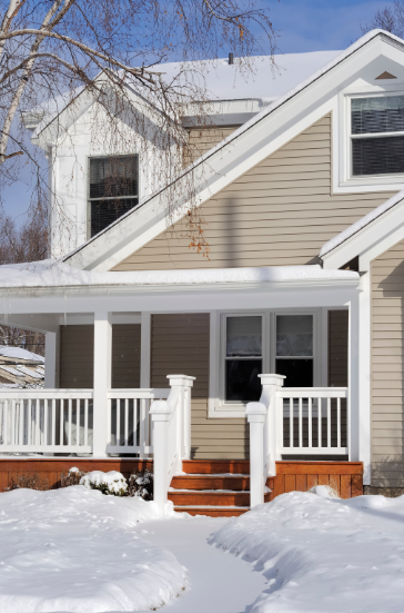 A house with a porch is covered in snow.