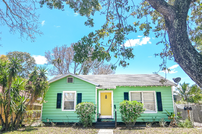 A green house with a yellow door and black shutters