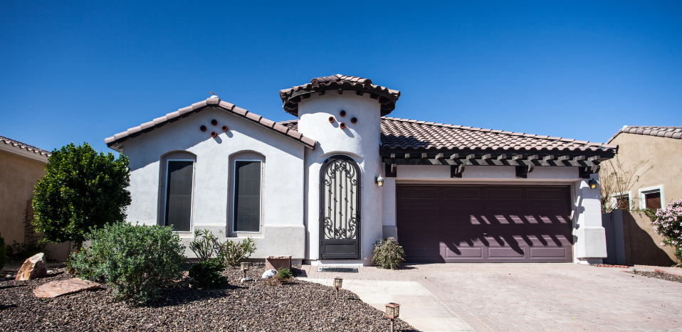 A white house with a brown garage door and a tile roof.