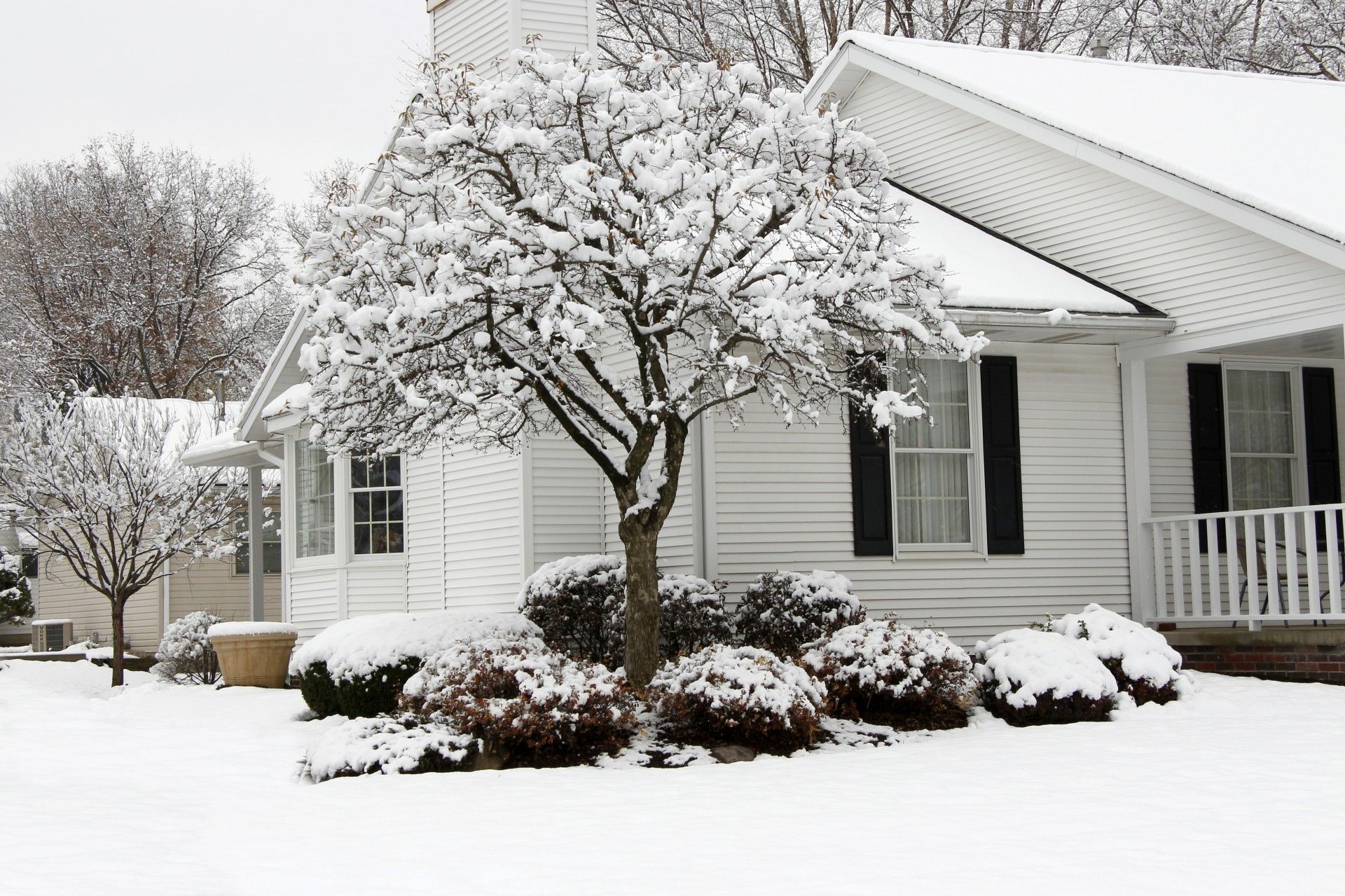 A white house with black shutters is covered in snow