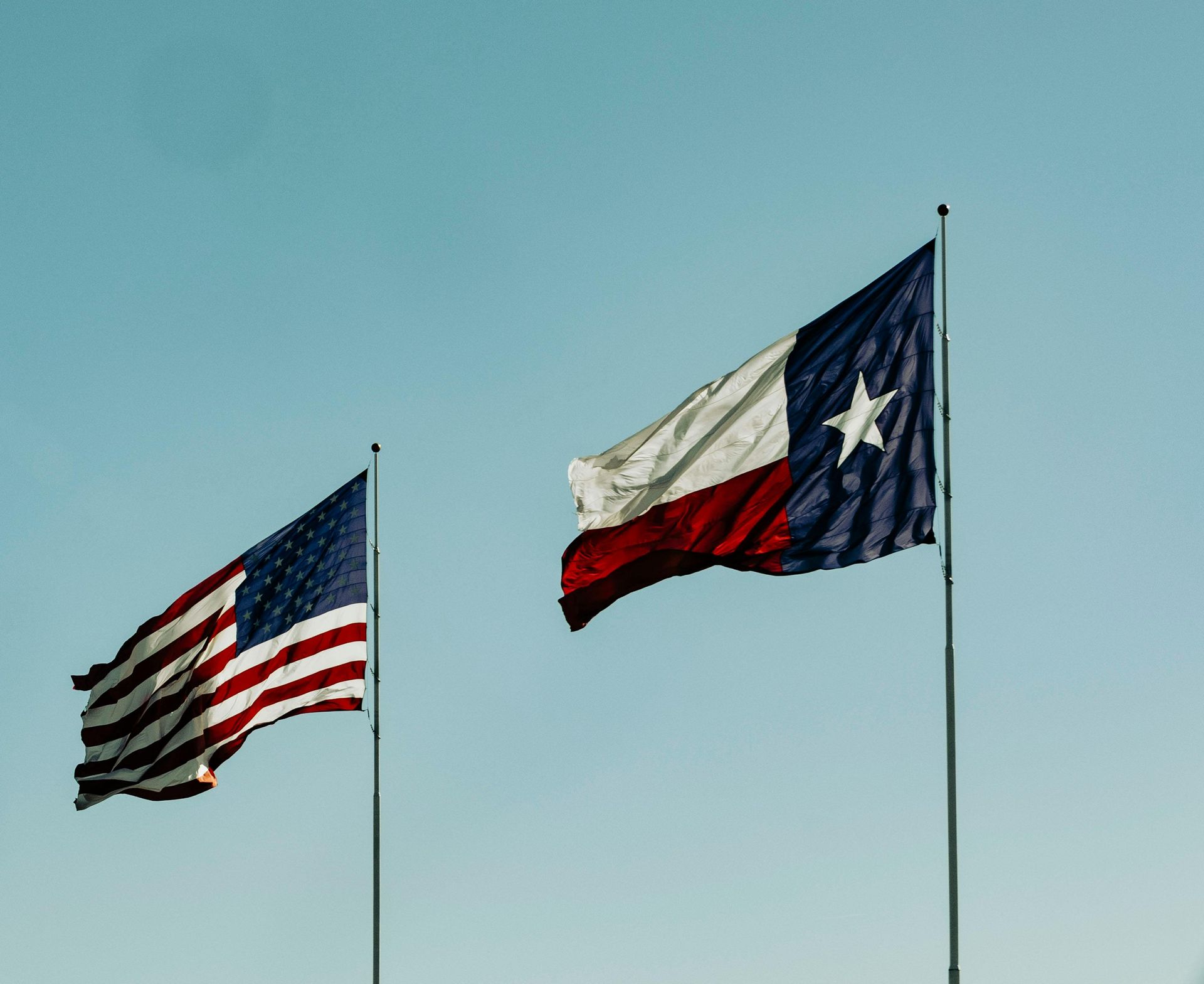 U.S. and Texas flags waving on tall poles against a clear blue sky