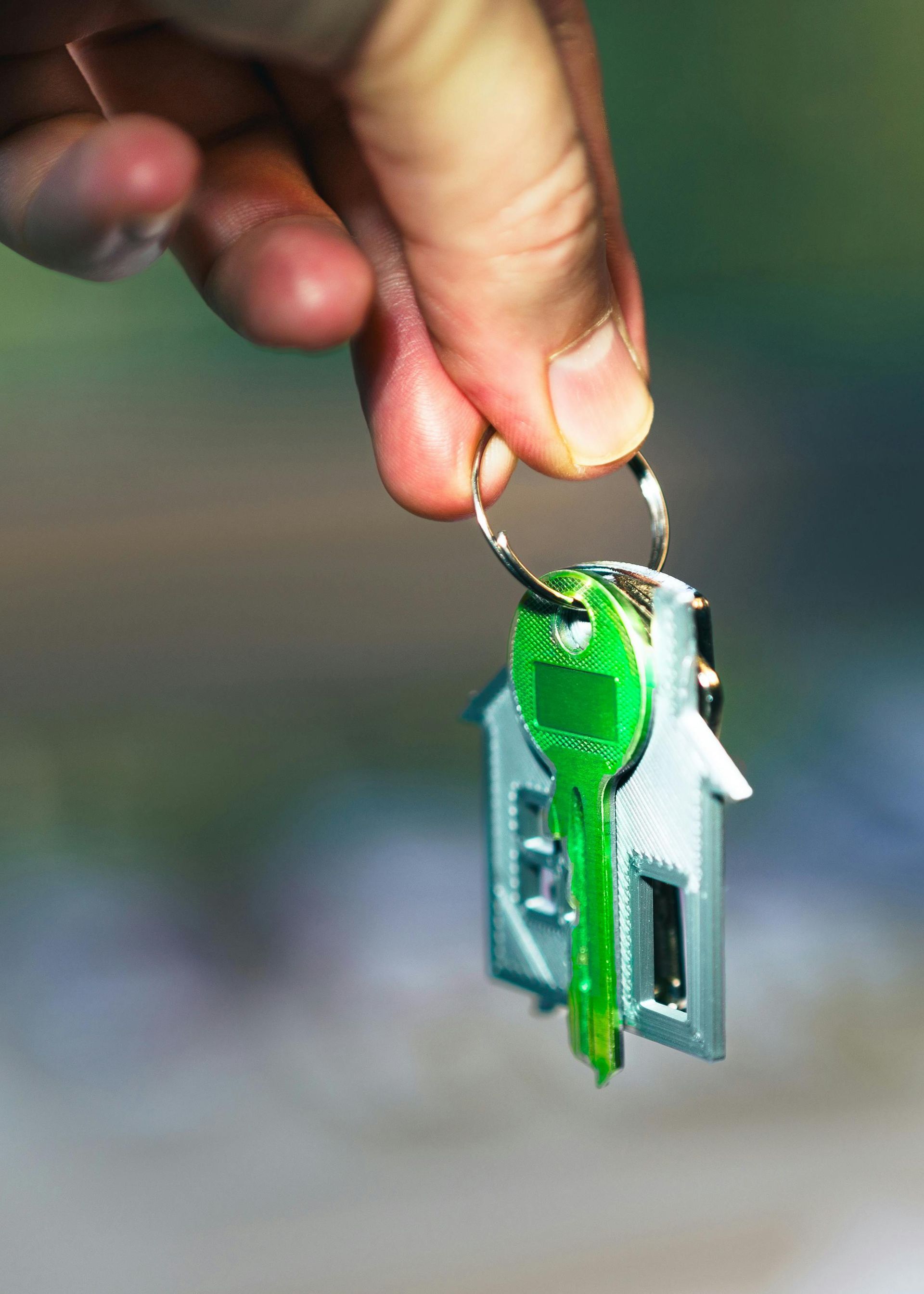 Hand holding a green house key attached to a small keychain ornament
