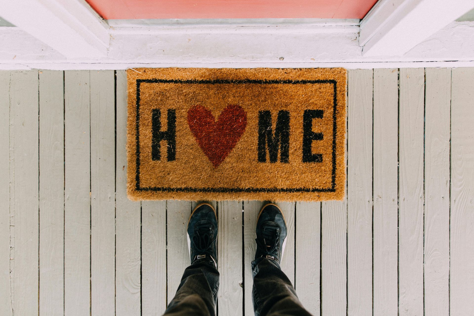 A person is standing in front of a door mat that says `` home '' with a heart on it.