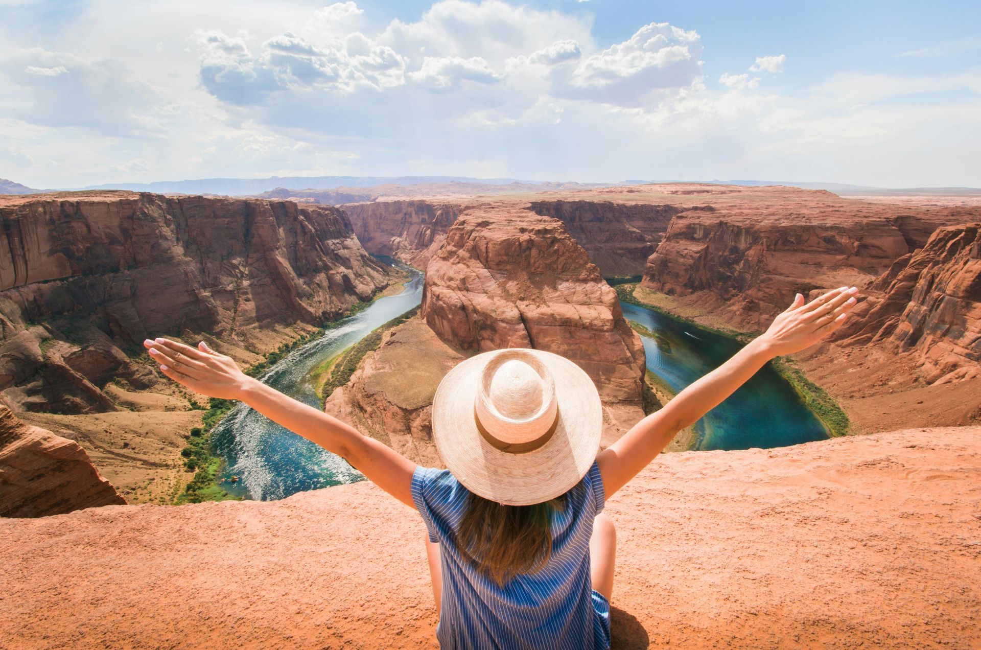 A woman is sitting on the edge of a canyon with her arms outstretched.