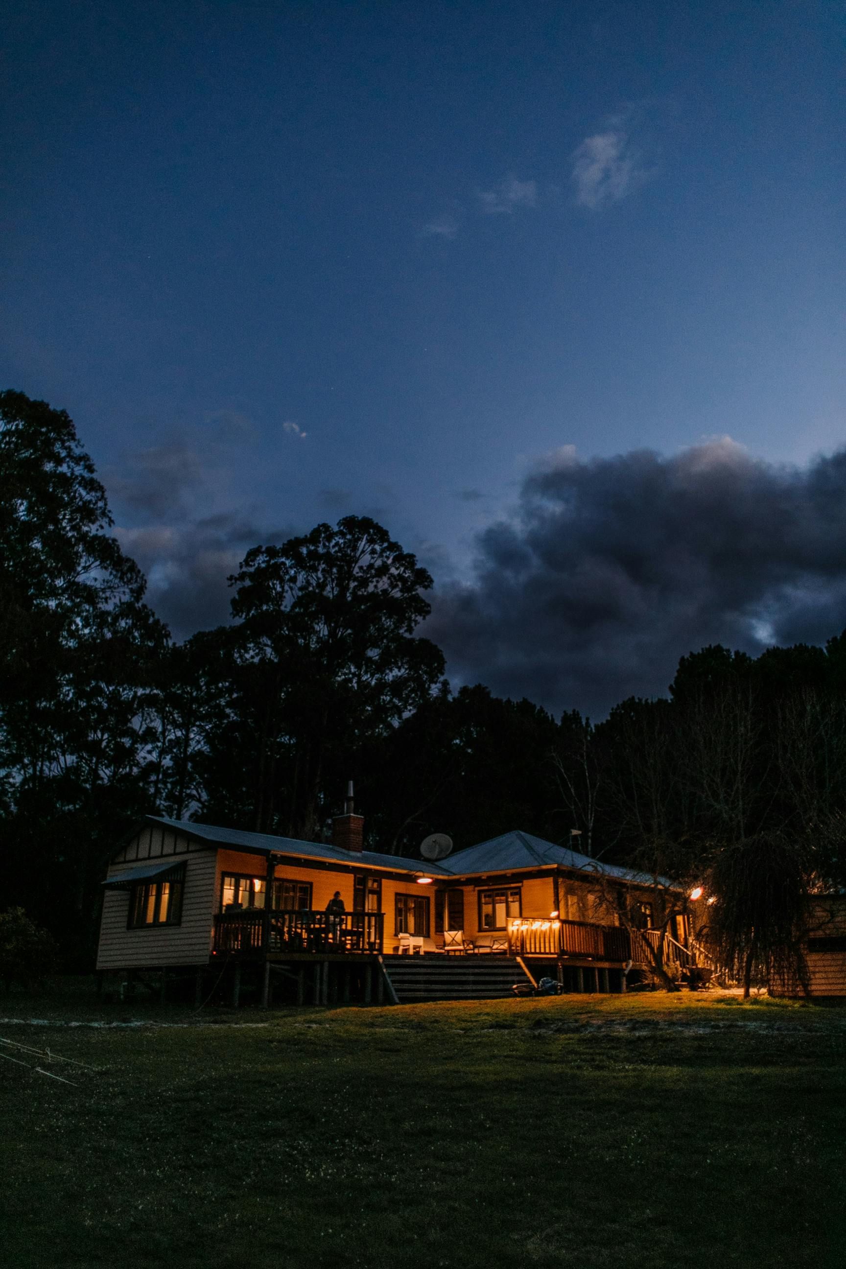 A house is lit up at night in a field with trees in the background.