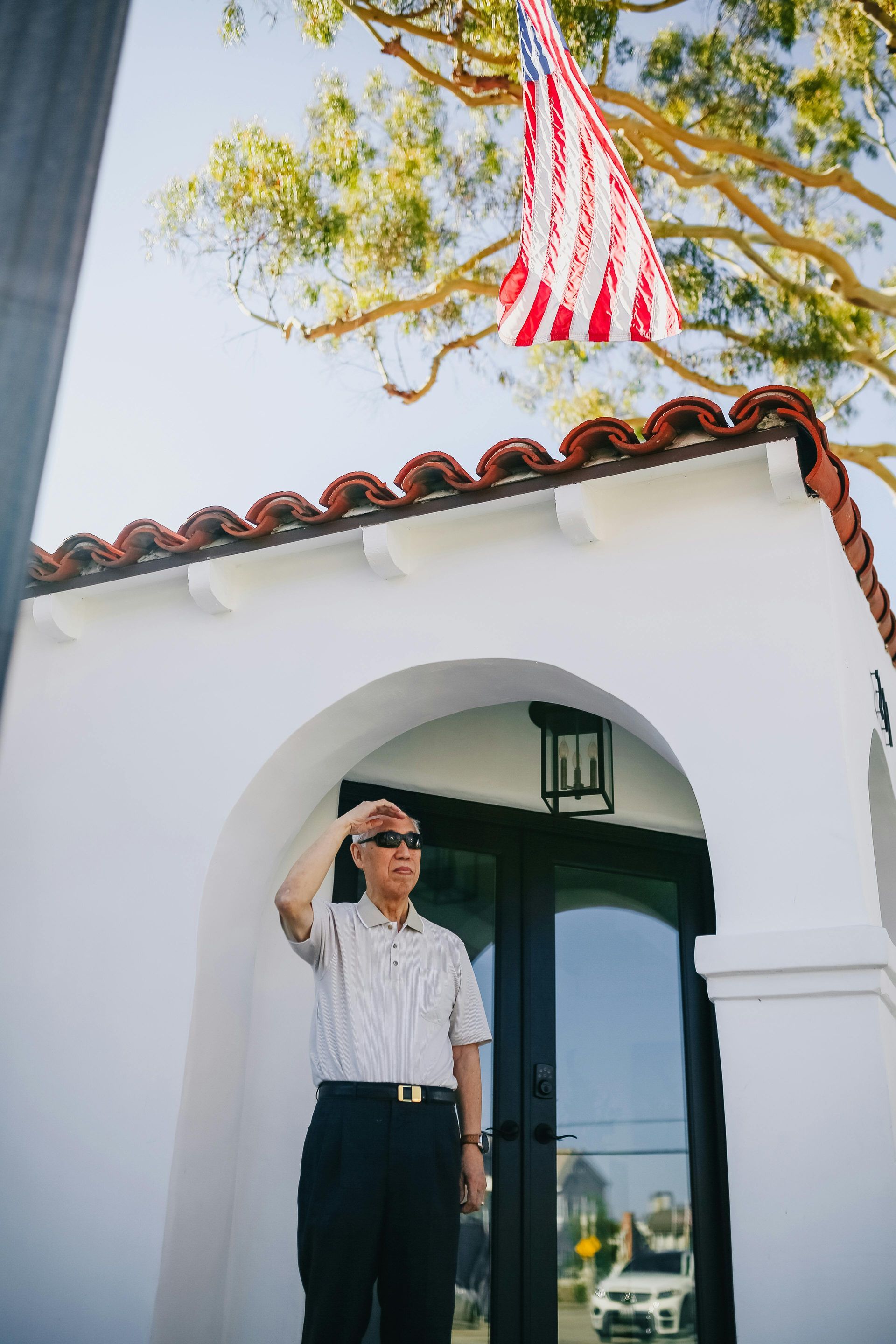 A man is saluting in front of a building with an american flag flying in the background.