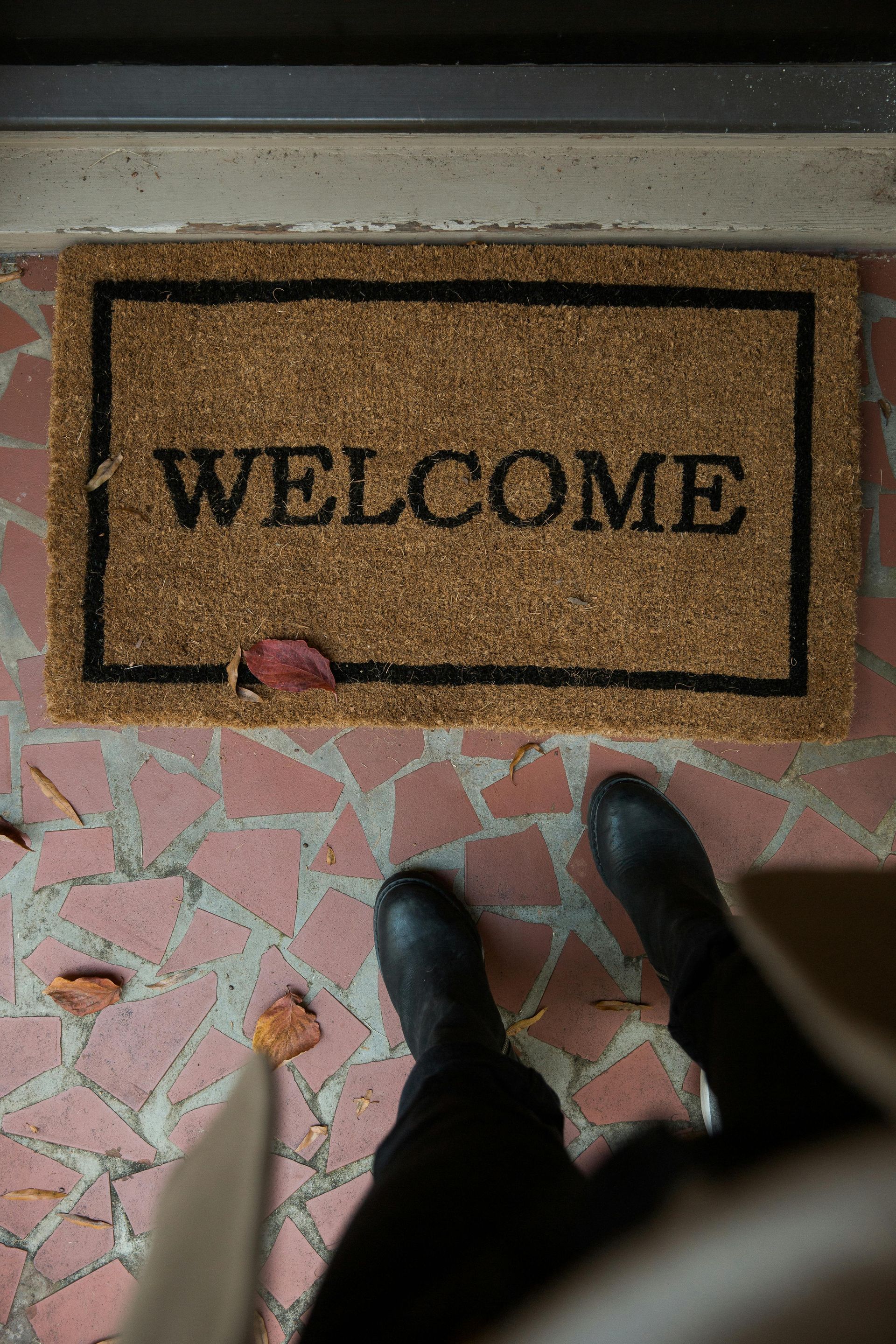 A person is standing in front of a welcome mat.