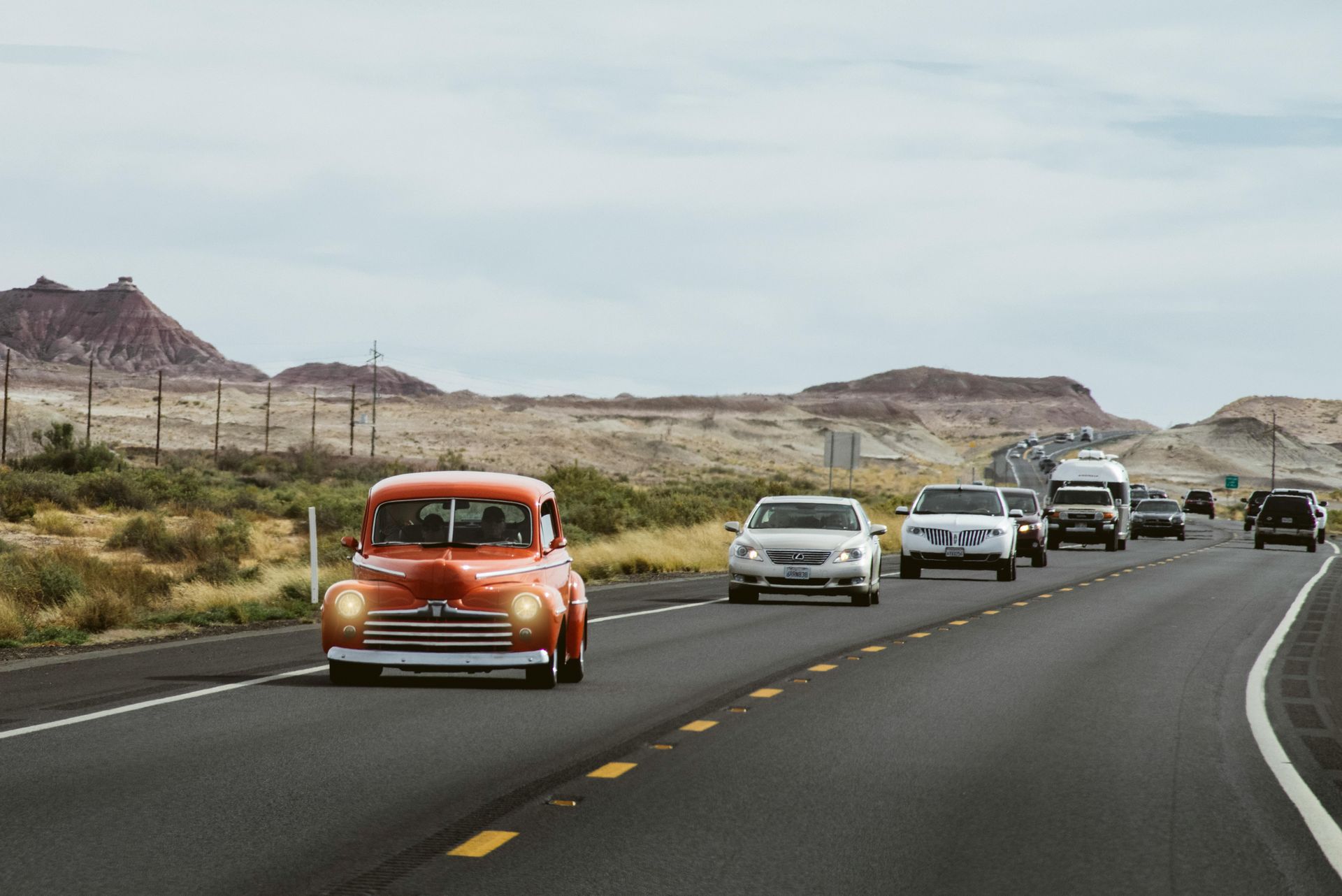 A row of cars are driving down a highway in the desert.