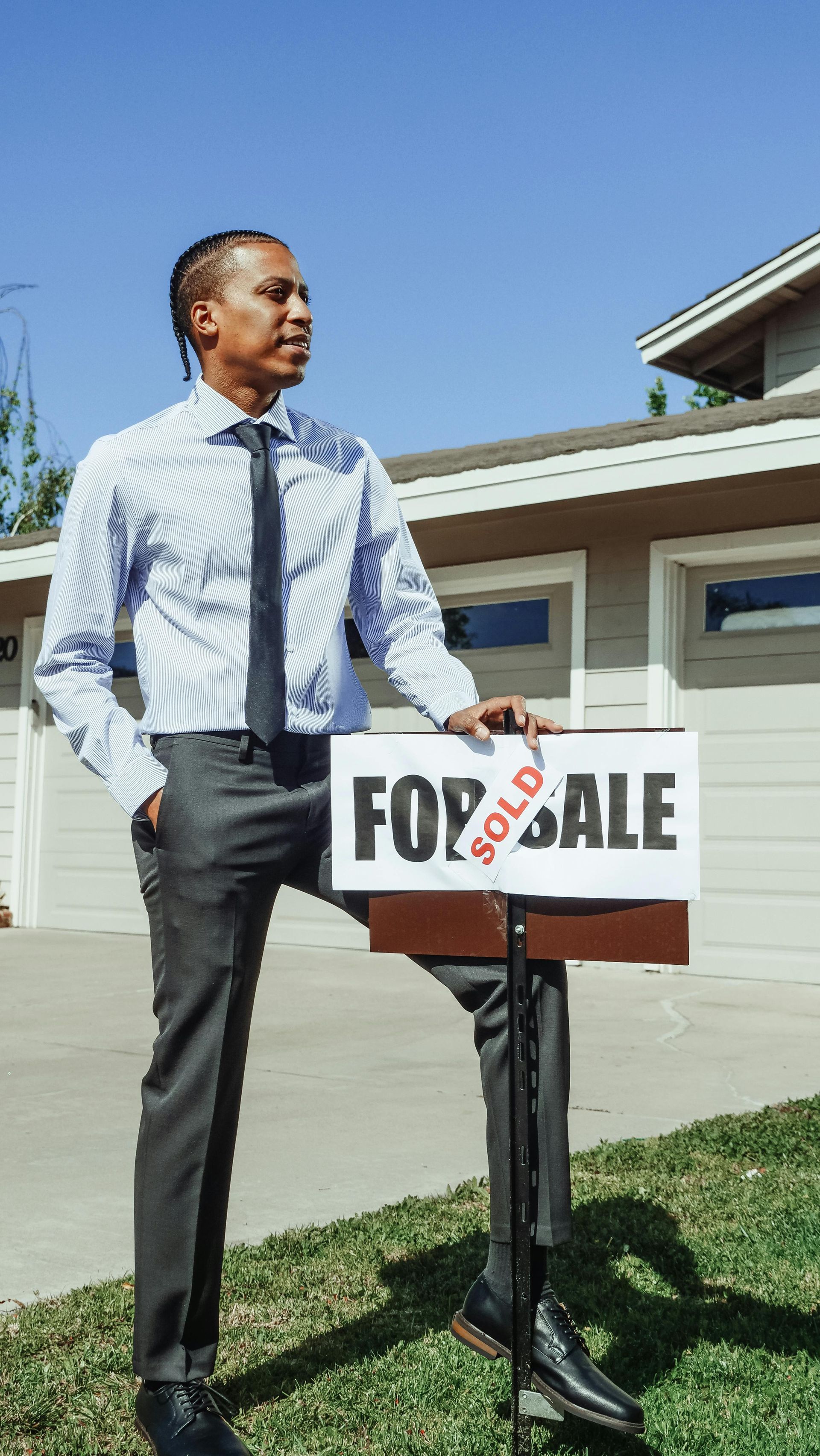 A man is standing in front of a house holding a sold sign.