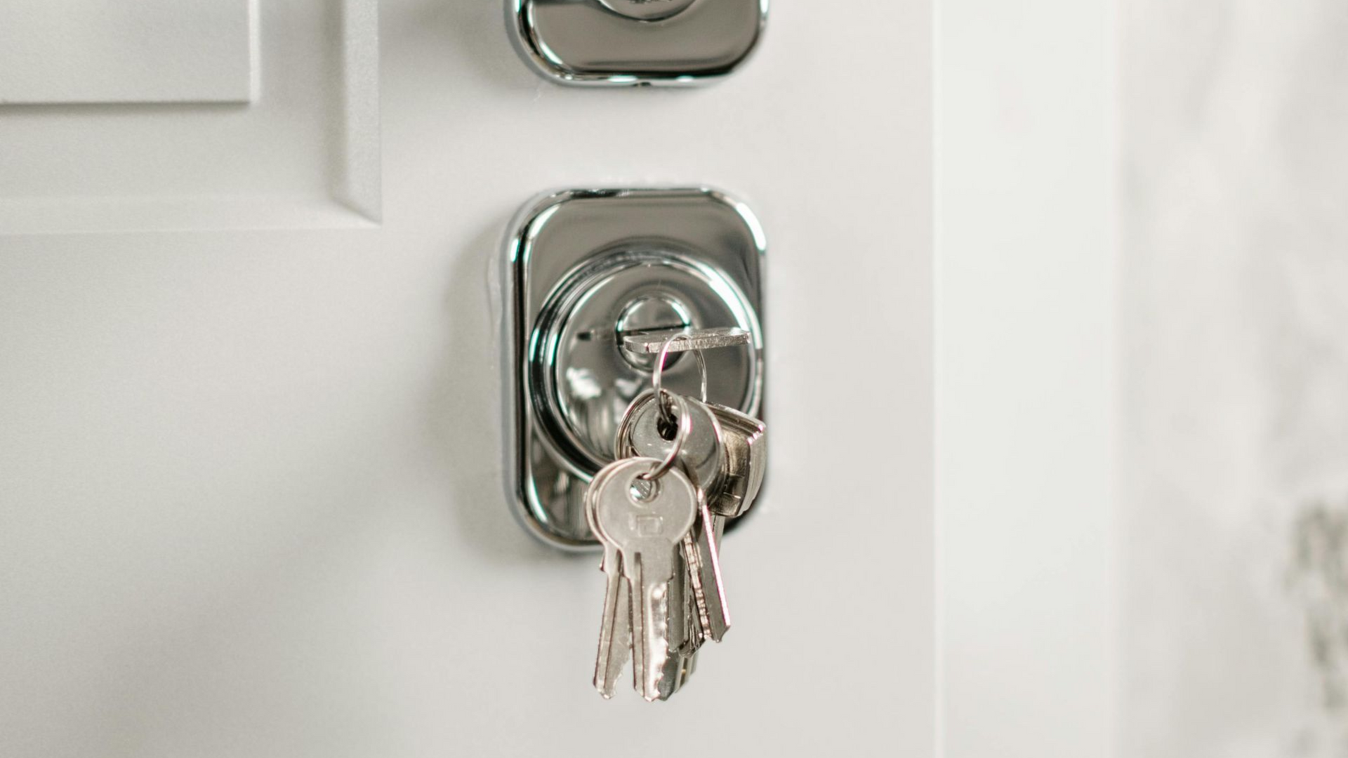 Keys in a silver lock on a white door