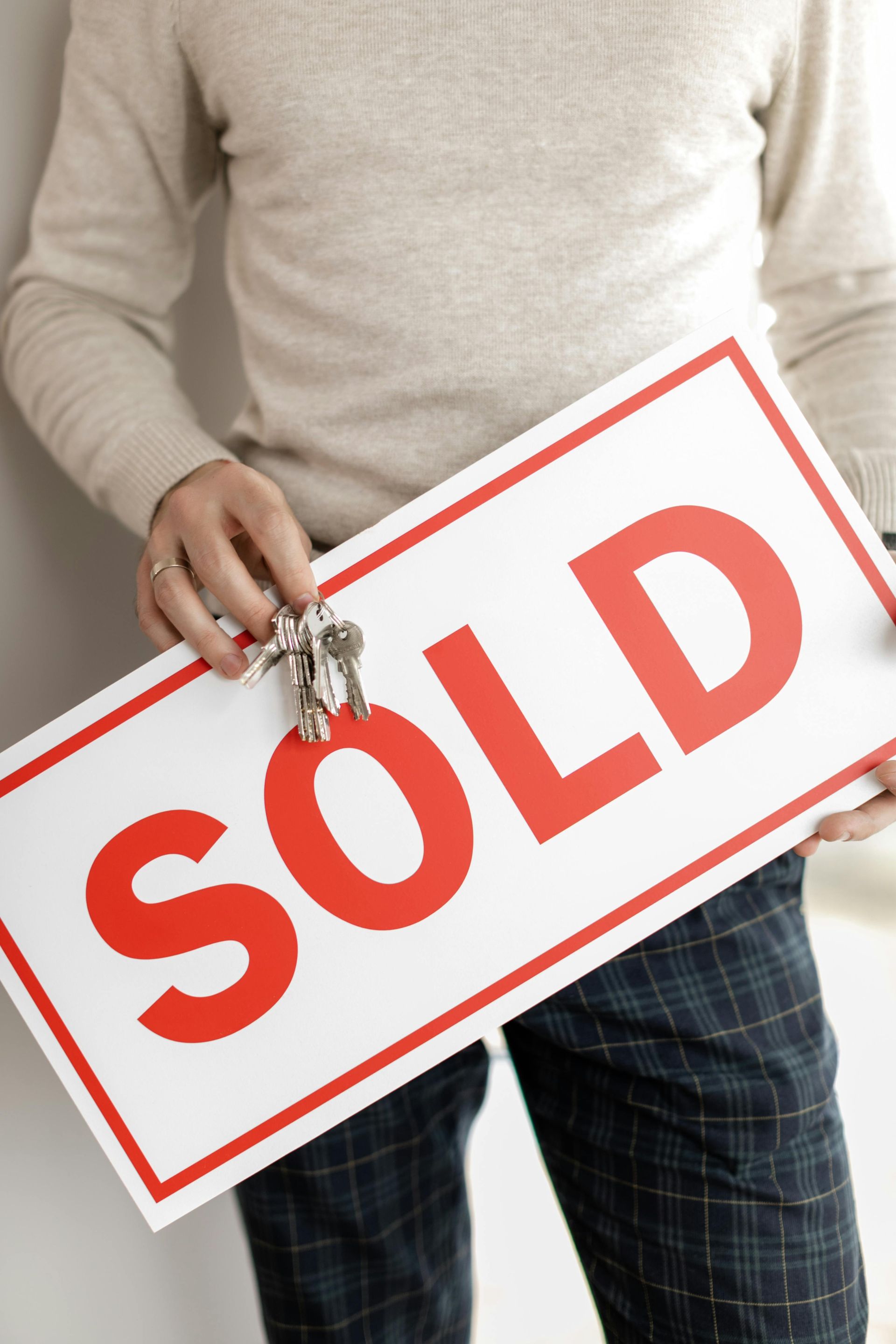 A man is holding a sold sign with keys attached to it