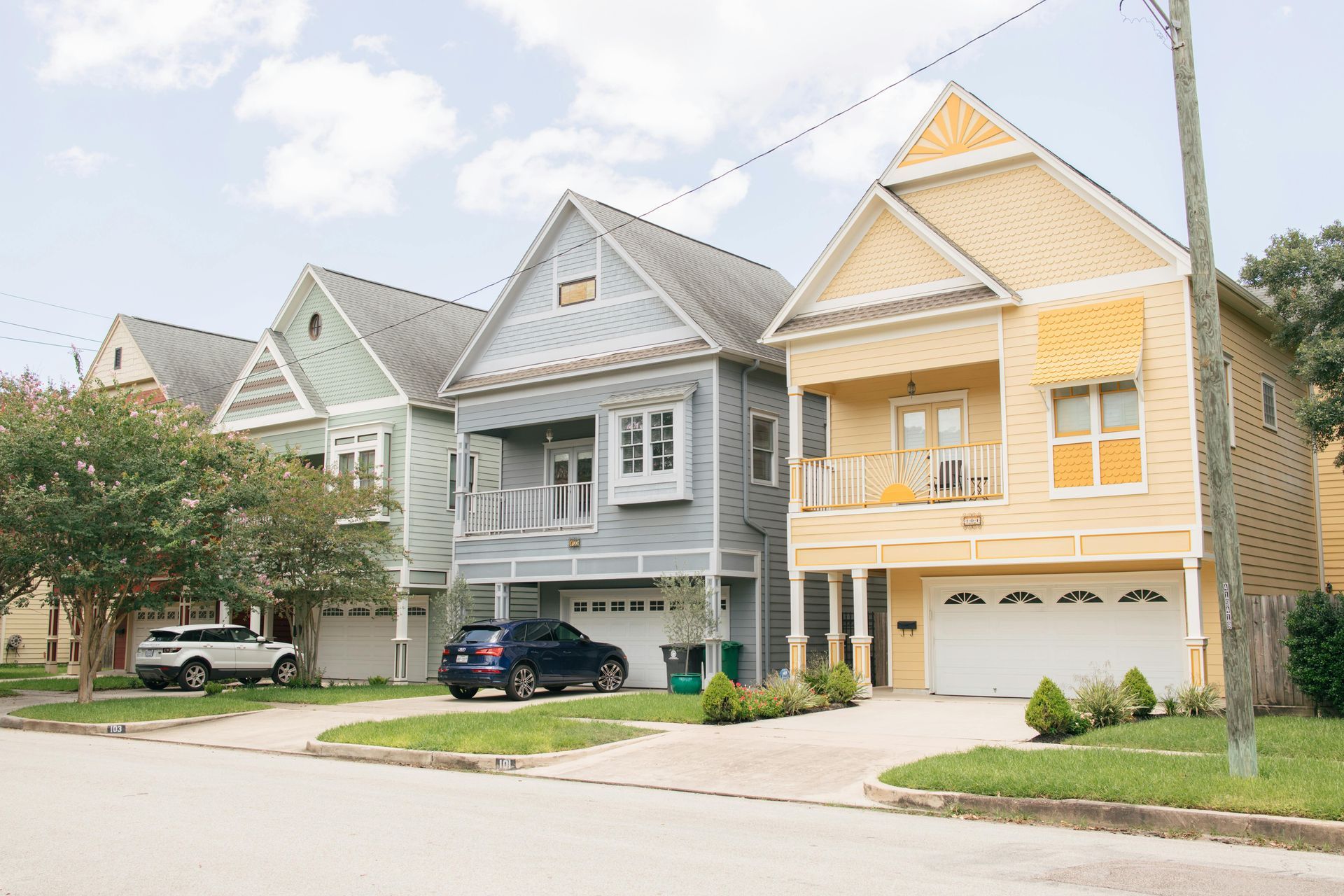 A row of three colorful houses on a residential street with cars parked in their driveways.