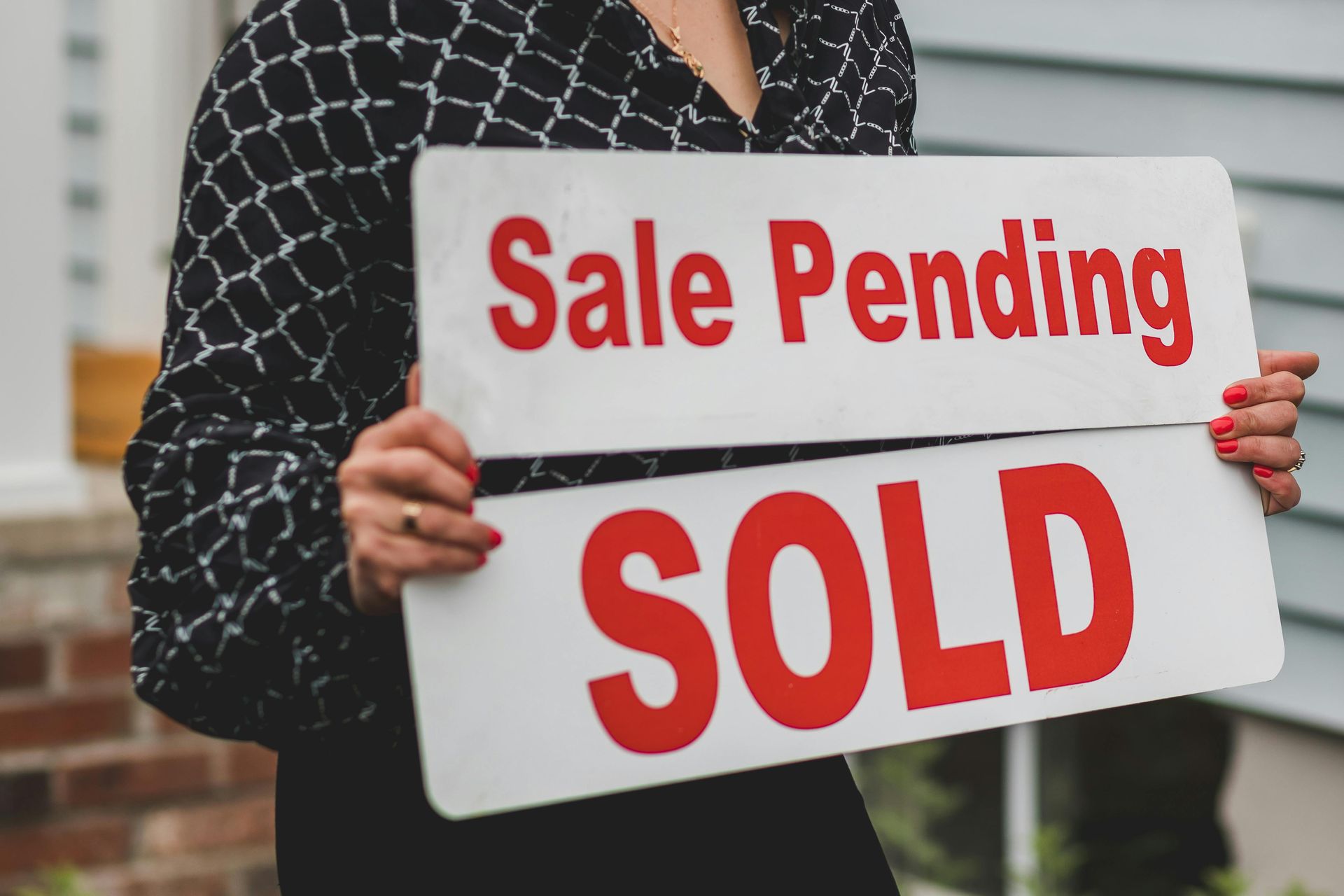 A woman is holding two signs that say sale pending and sold.