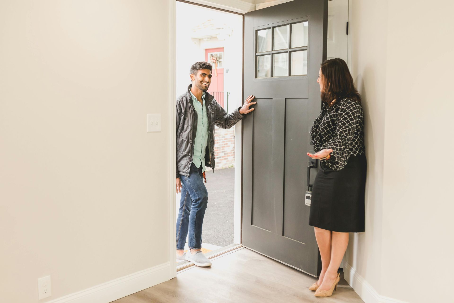 Man opens a door for a woman; they stand in a neutral-colored doorway.
