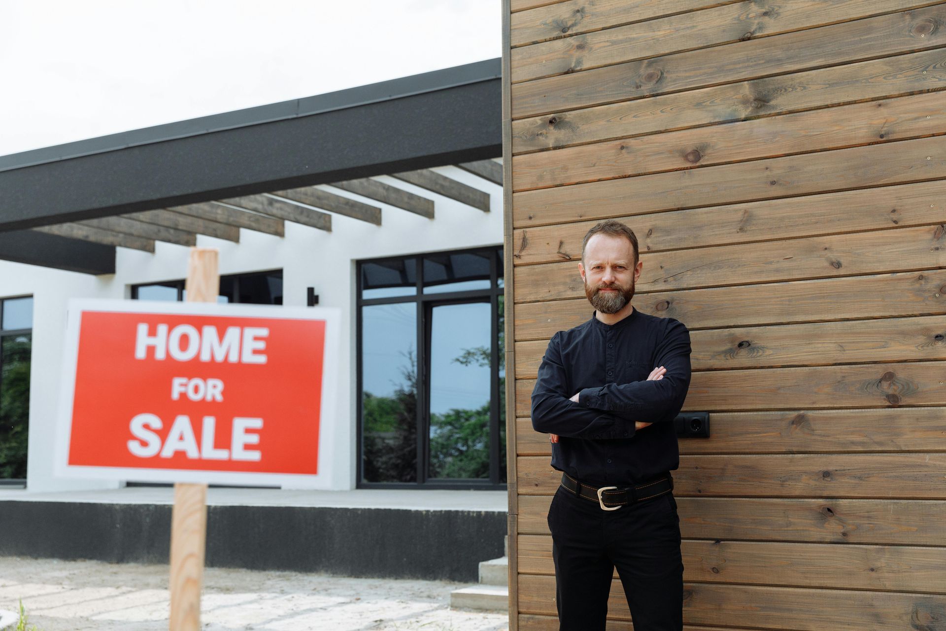 A man is standing in front of a house with a home for sale sign.