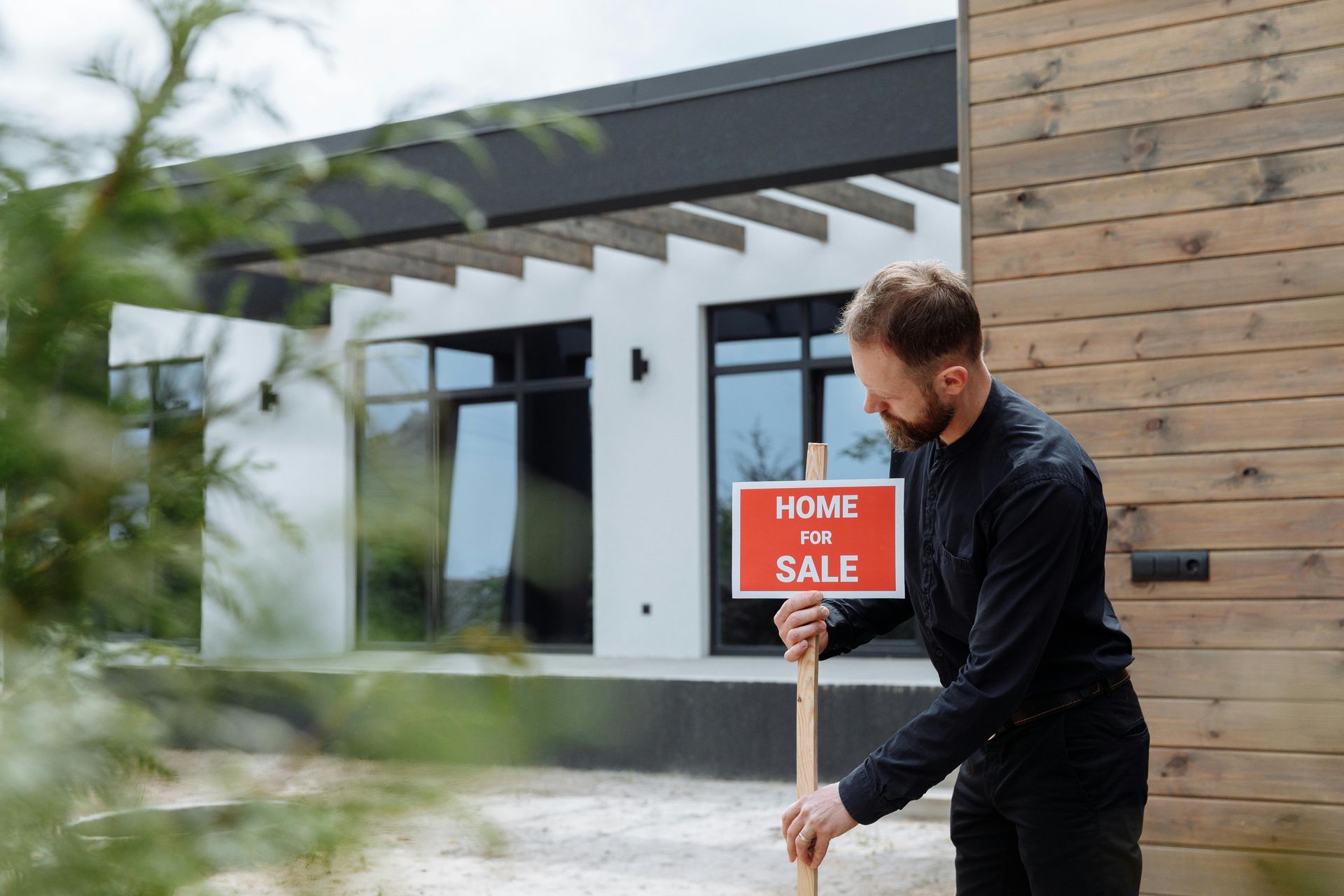 A man is holding a home for sale sign in front of a house.