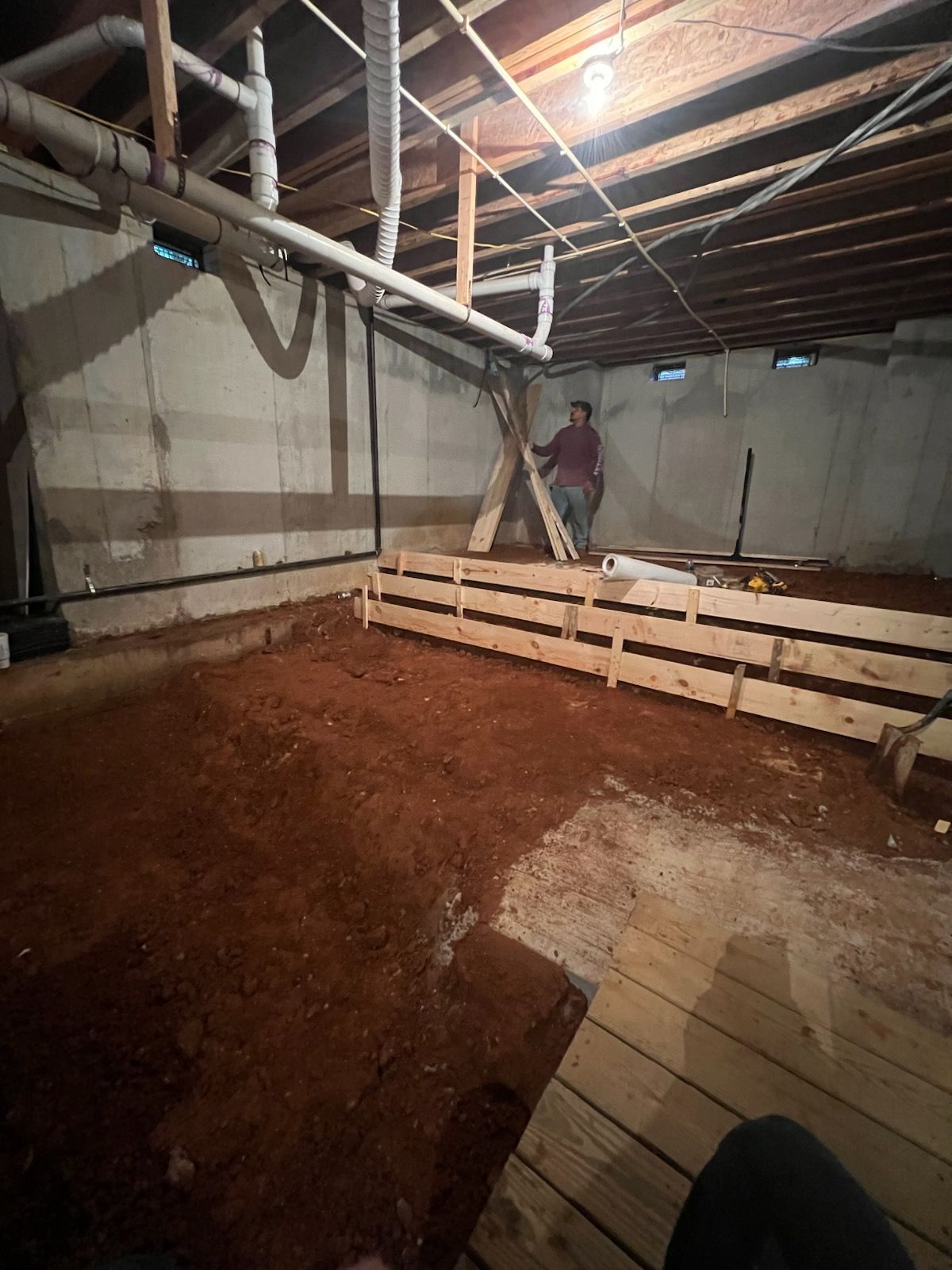 Basement under construction with wooden forms, red dirt floor, and person standing near a support. Basement under construction with wooden forms, red dirt floor, and person standing near a support.