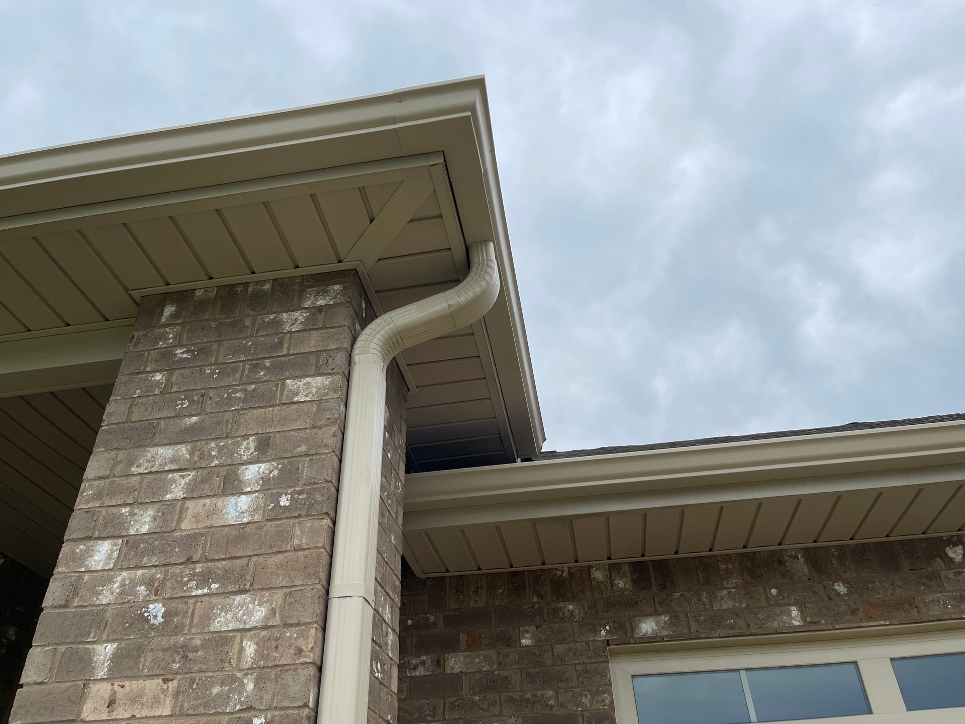 Person in safety vest cleans roof gutter, wearing gloves and boots.