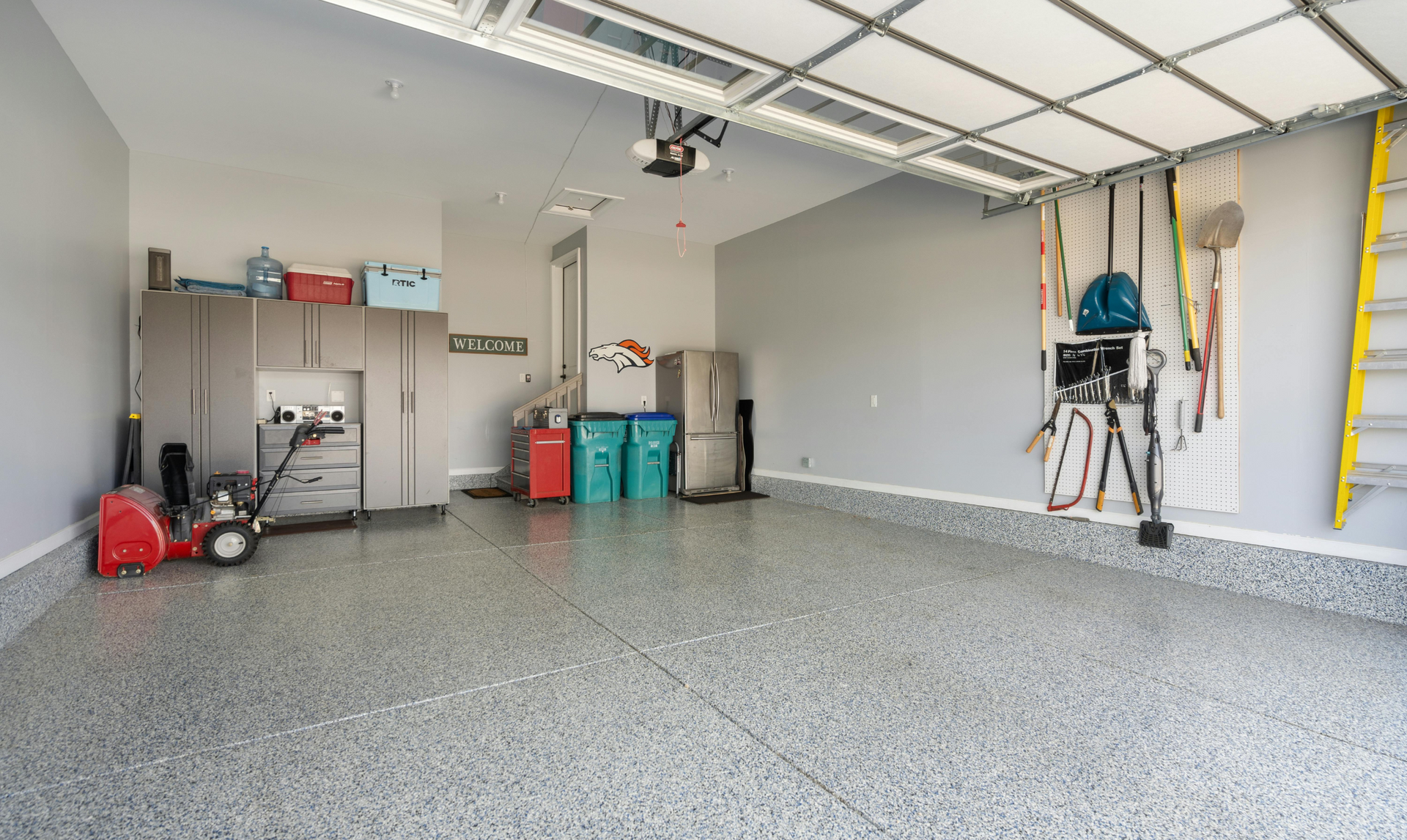 Spacious garage with gray cabinets, epoxy floor, and various tools hanging on the wall.