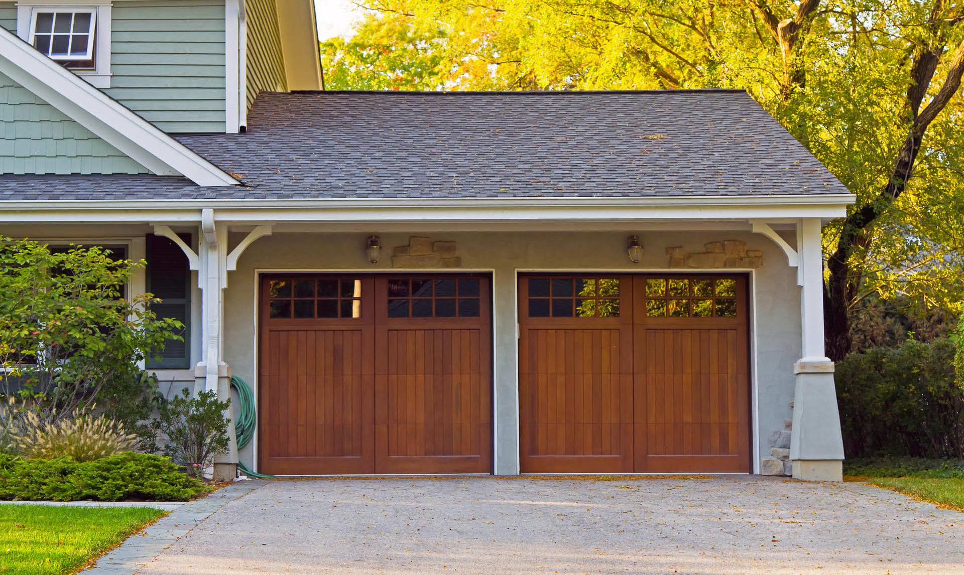 Brown wooden garage doors on a house with a gray roof and concrete driveway.