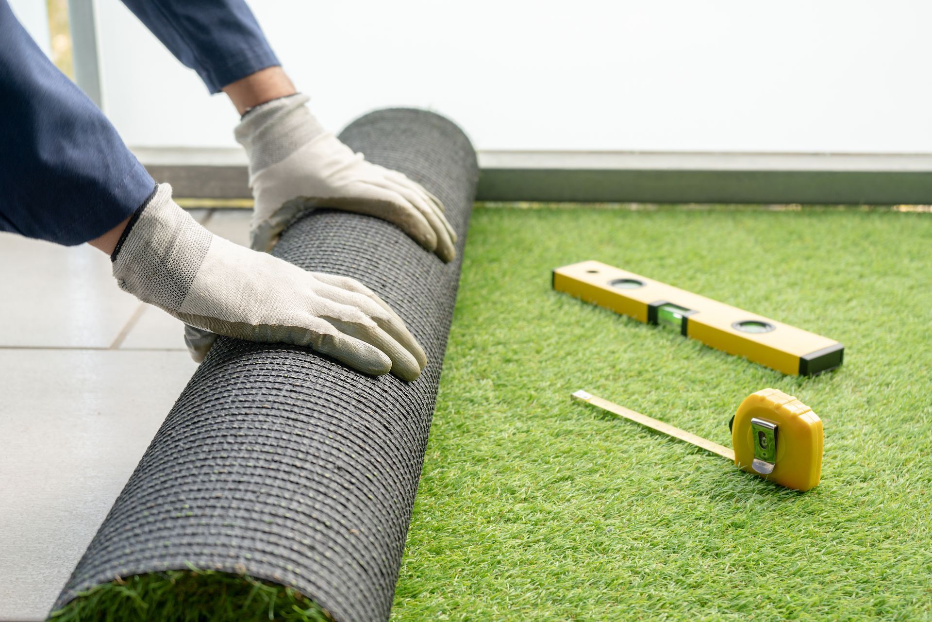 Person rolling out artificial turf, with level and measuring tape.