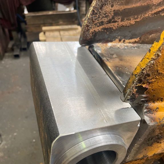 A close-up view of a freshly machined, smooth steel rectangular component fitted against a weathered yellow metal frame.