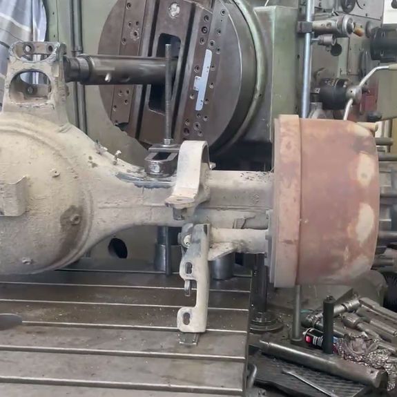 A dirty automotive rear axle assembly mounted on a large industrial milling machine in a workshop.