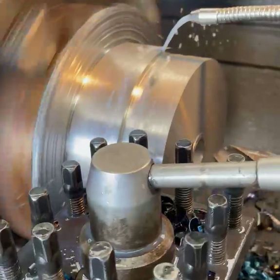 A metal lathe cuts a cylindrical part with a cooling fluid stream directed at the cutting tool contact point.