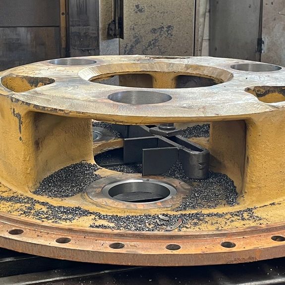 A yellow industrial metal flange component sits on a work surface, scattered with dark metal shavings from recent machining.