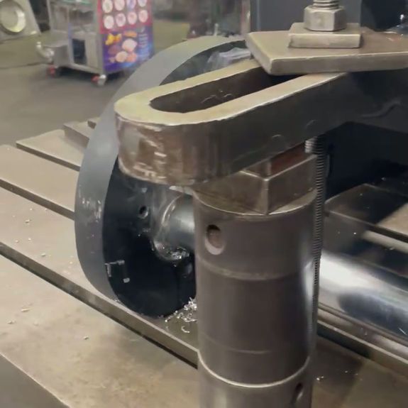 Close-up of a metal machining tool clamped onto a workshop table, with a circular wheel and metal shavings nearby.