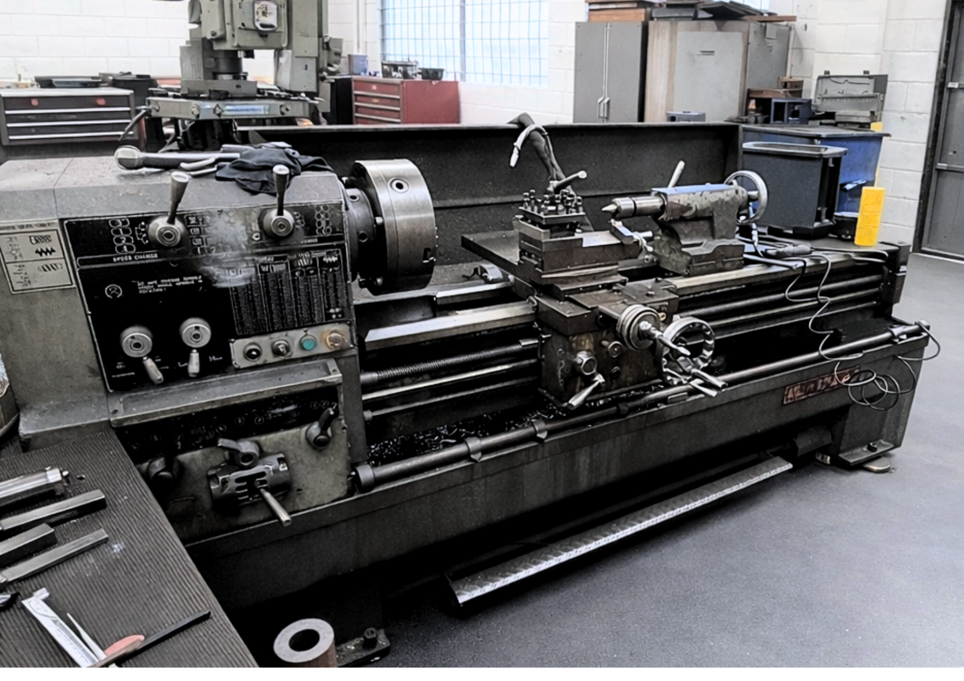 Large metal lathe in a machine shop with gray walls, windows, and industrial equipment. Large metal lathe in a machine shop with gray walls, windows, and industrial equipment.