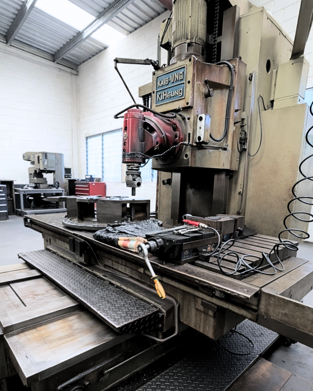 Industrial workshop with a large vertical milling machine and metal parts on a workbench. Industrial workshop with a large vertical milling machine and metal parts on a workbench.