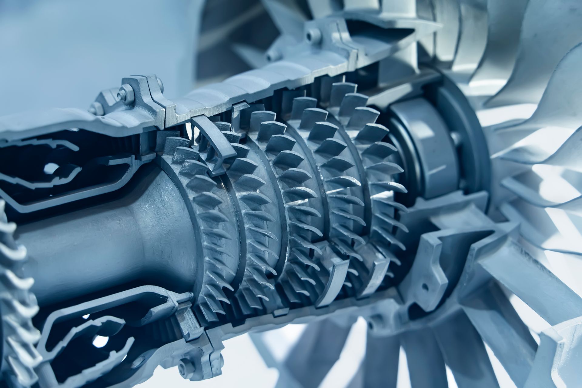 A close-up, cutaway view of a jet engine's internal compressor blades and turbine rotors, presented in a monochromatic blue.