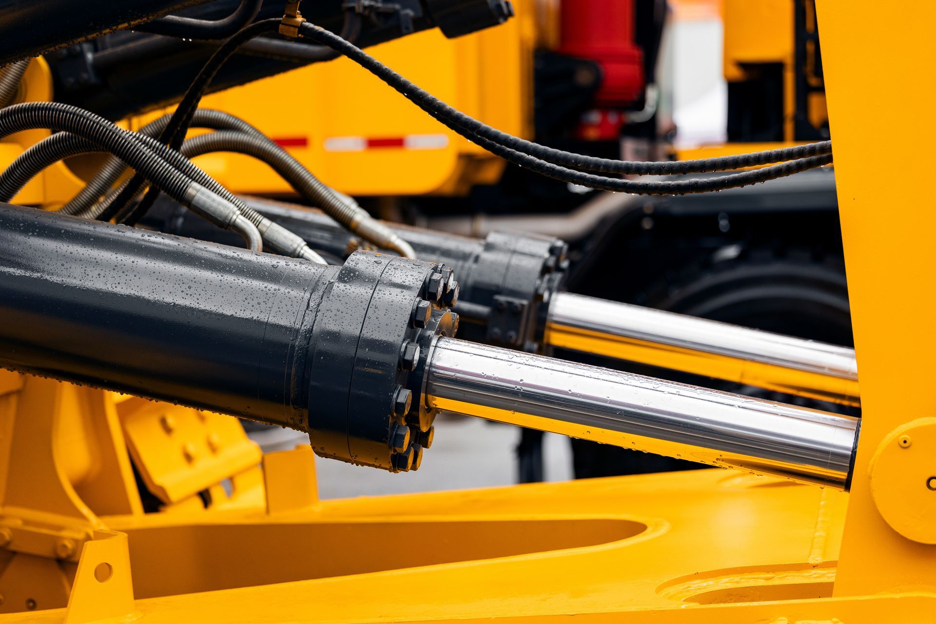 Close-up of polished hydraulic cylinders and black metal housing on a yellow construction vehicle.