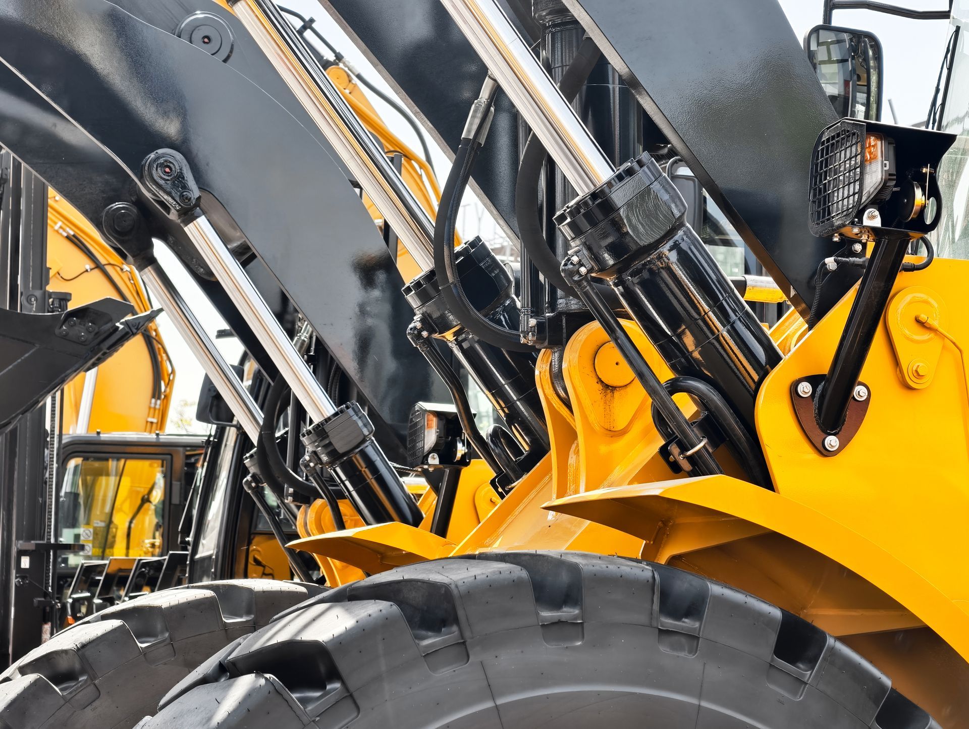 A close-up view of the yellow metal arm and hydraulic cylinders of a construction vehicle above a large rubber tire.