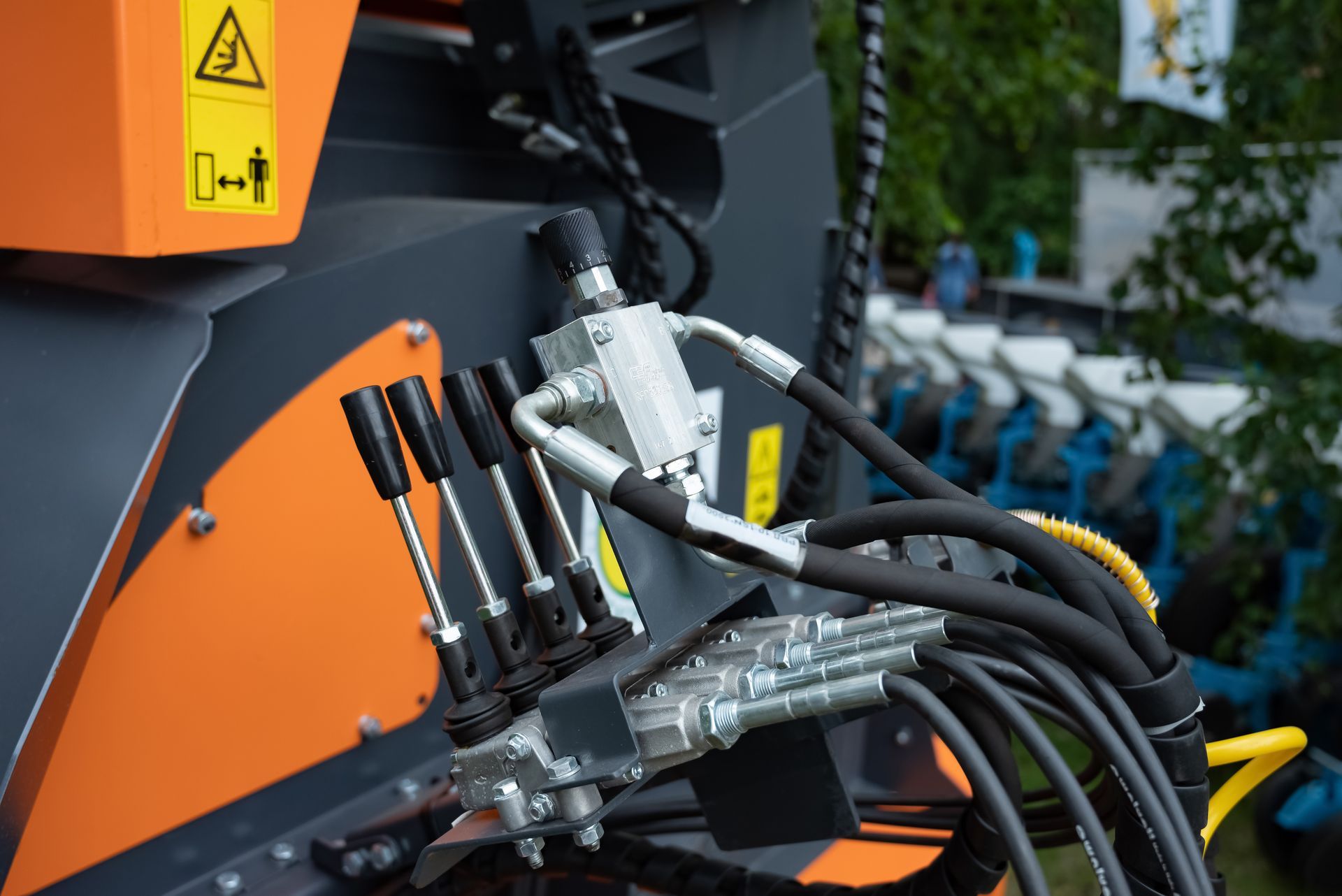Hydraulic control levers and hoses on industrial orange and grey machinery.