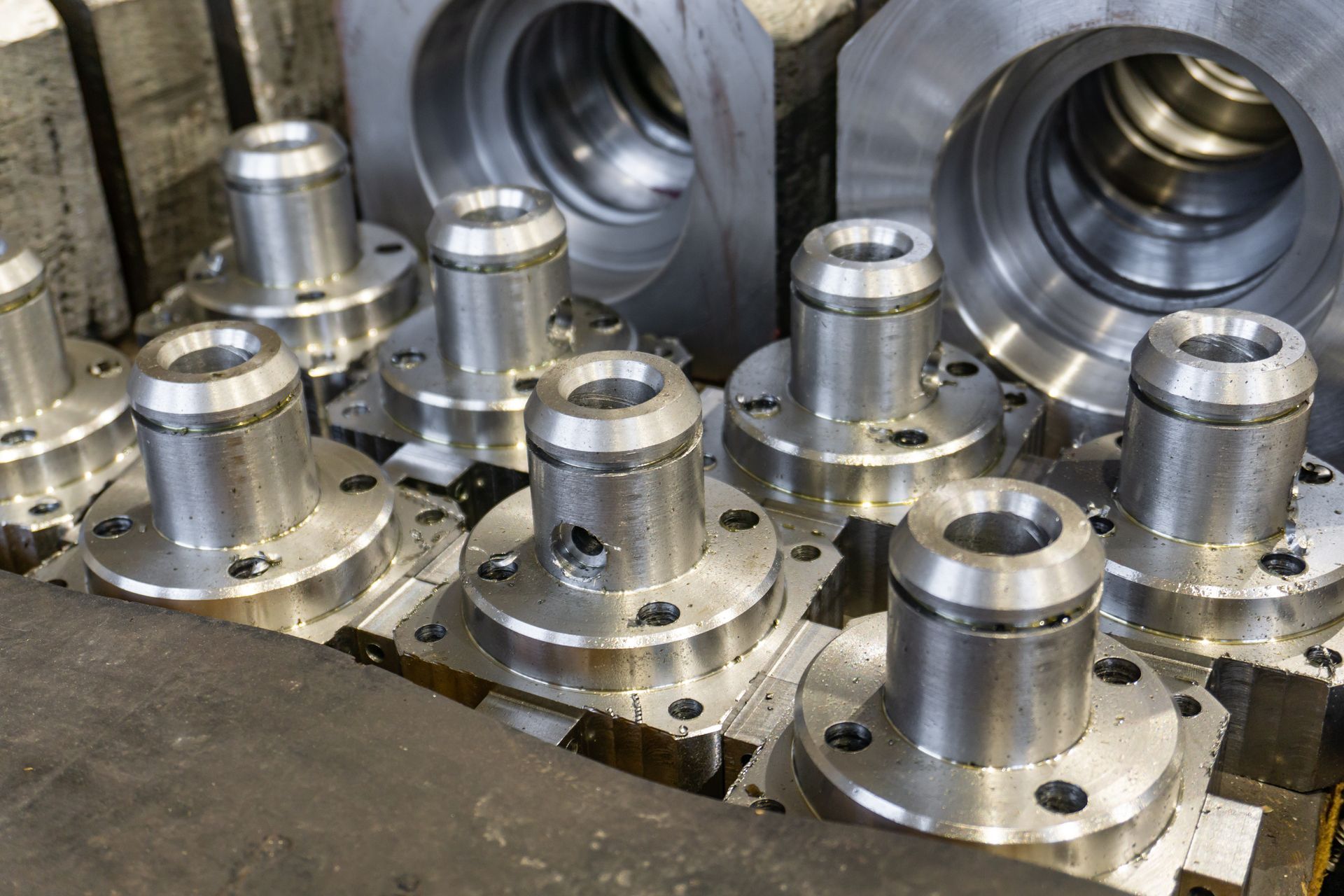 Several machined metal flanged parts sit arranged on a flat surface in a factory or workshop setting.
