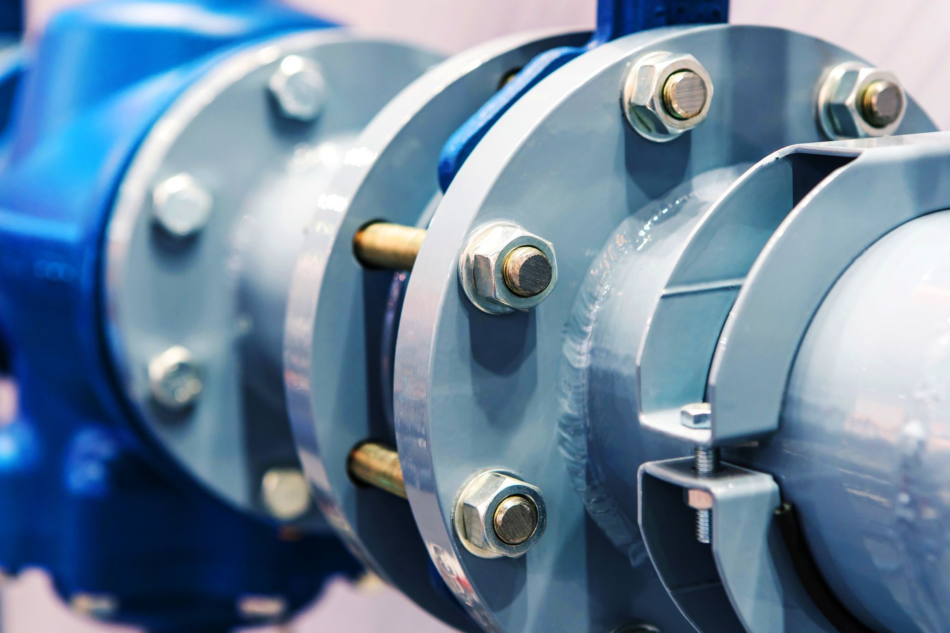 A close-up view of industrial steel flanges and pipes connected with bolts and nuts, painted in grey and blue.
