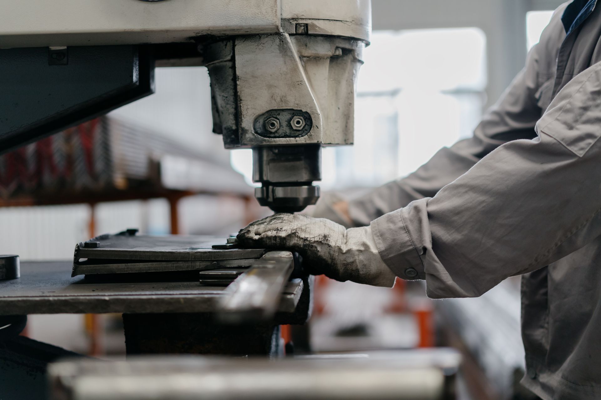 A worker wearing protective gloves operates an industrial metal press in a workshop.