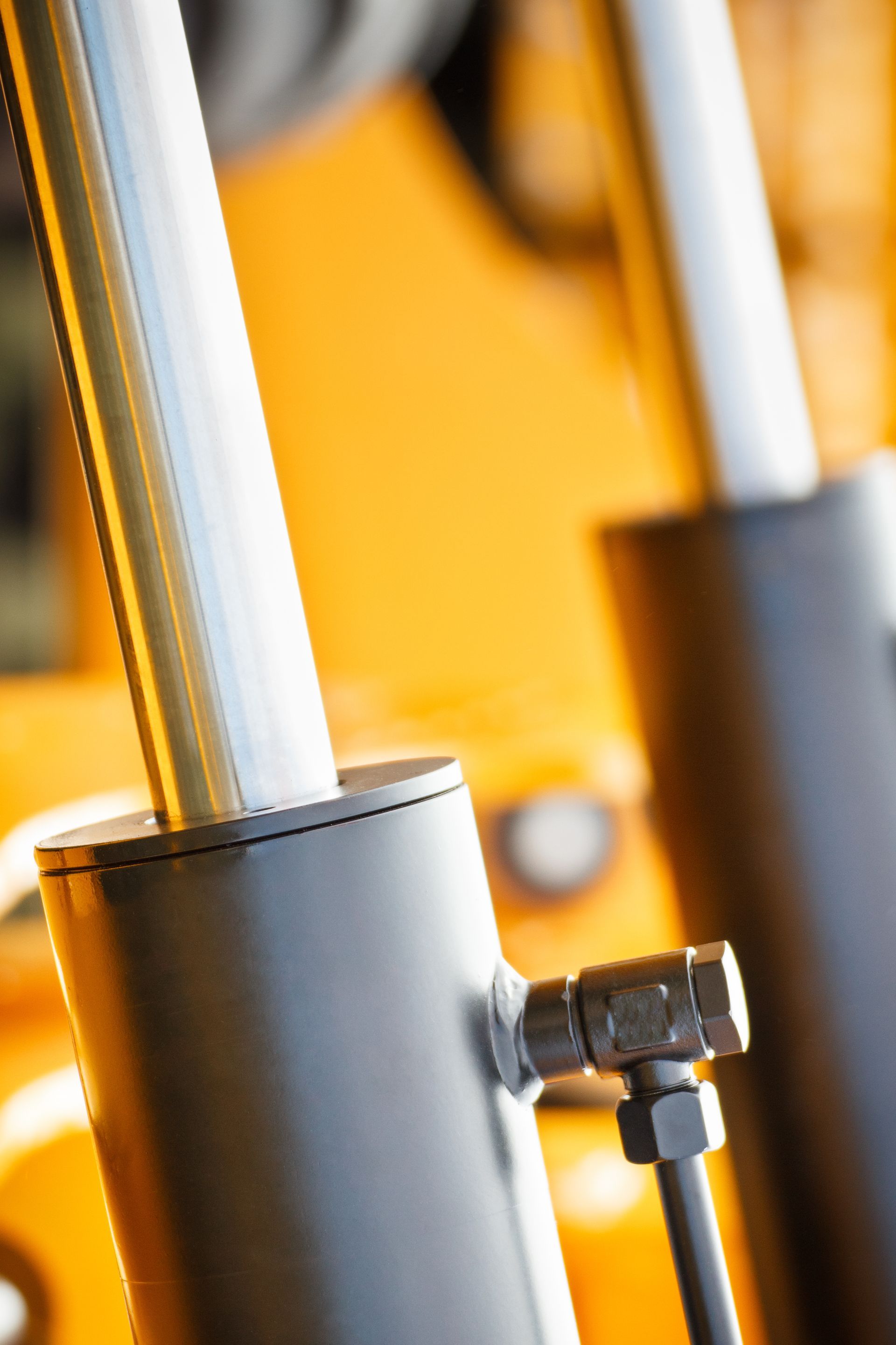 Close-up of two metallic hydraulic piston rods emerging from black cylindrical housings on yellow machinery.