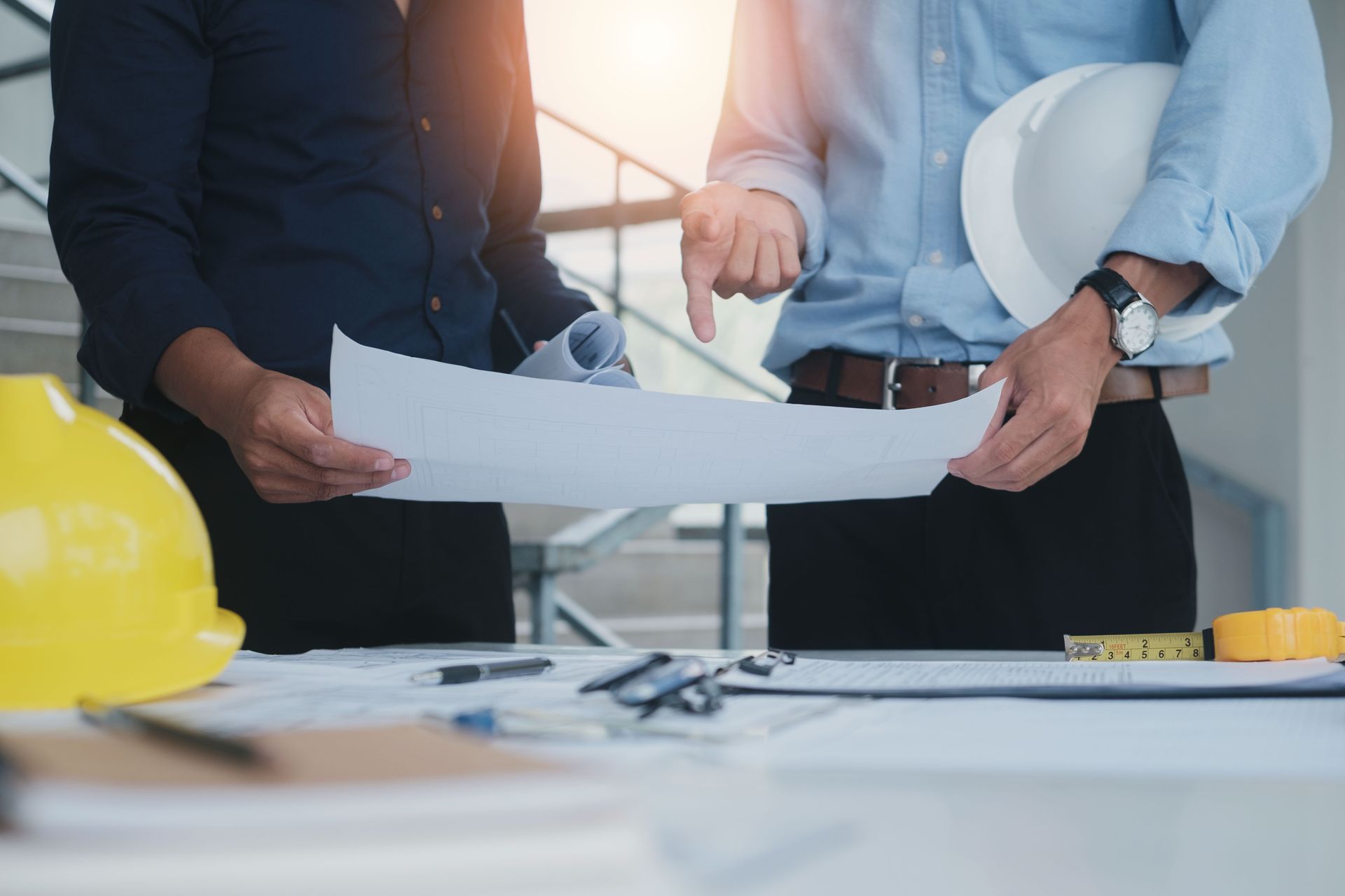 Two professionals in a bright workspace reviewing architectural blueprints together, one pointing at the documents.