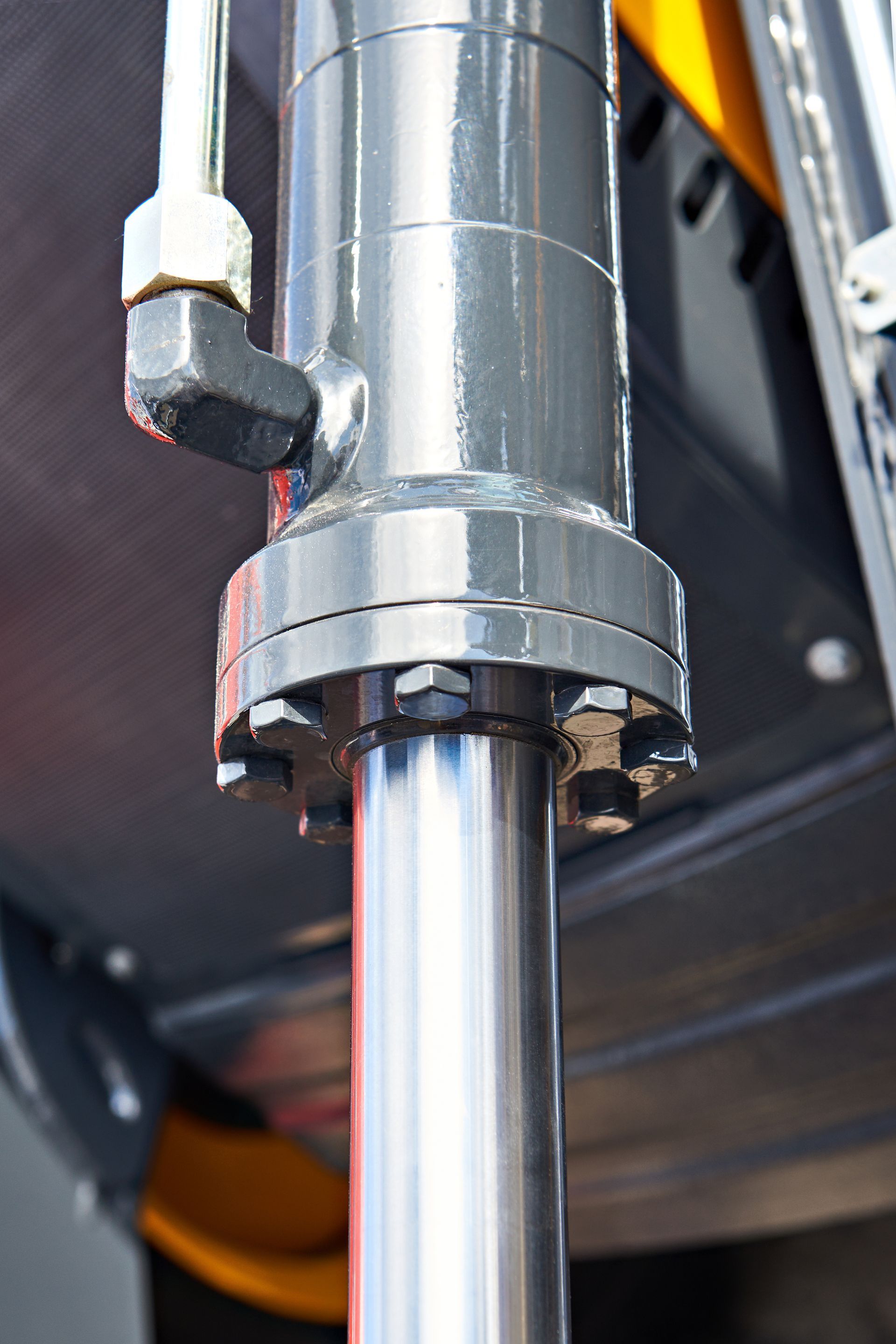 A close-up view of a gray, cylindrical hydraulic piston and rod with a metal connector and bolts attached.